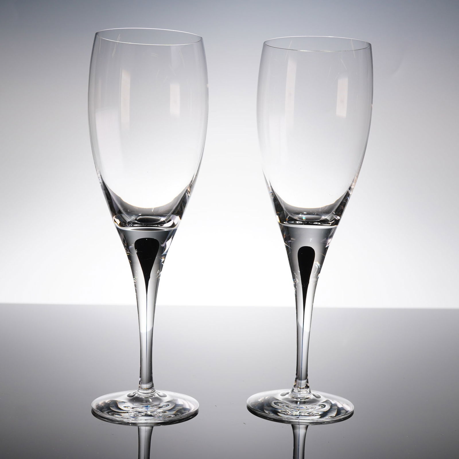 A Pair of Orrefors Intermezzo Black Champagne Flutes: A pair of contemporary crystal glasses by Orrefors in the Intermezzo Black patern. Each glass features a modern, sleek design with an elongated, tulip-shaped bowl set upon a slender stem and plain cir
