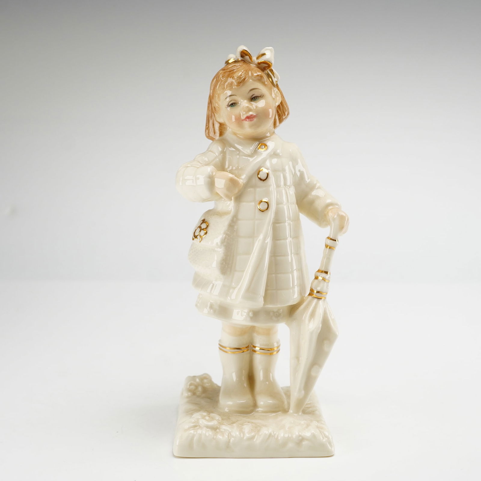 Royal Doulton Figurine, After the Rain HN4226: Royal Doulton from The Ivory and Gold Collection, modeled by Nada M. Pedley. The figure depicts a young girl in a quilted ivory-colored coat with a shoulder bag and boots, accented with gold-toned det