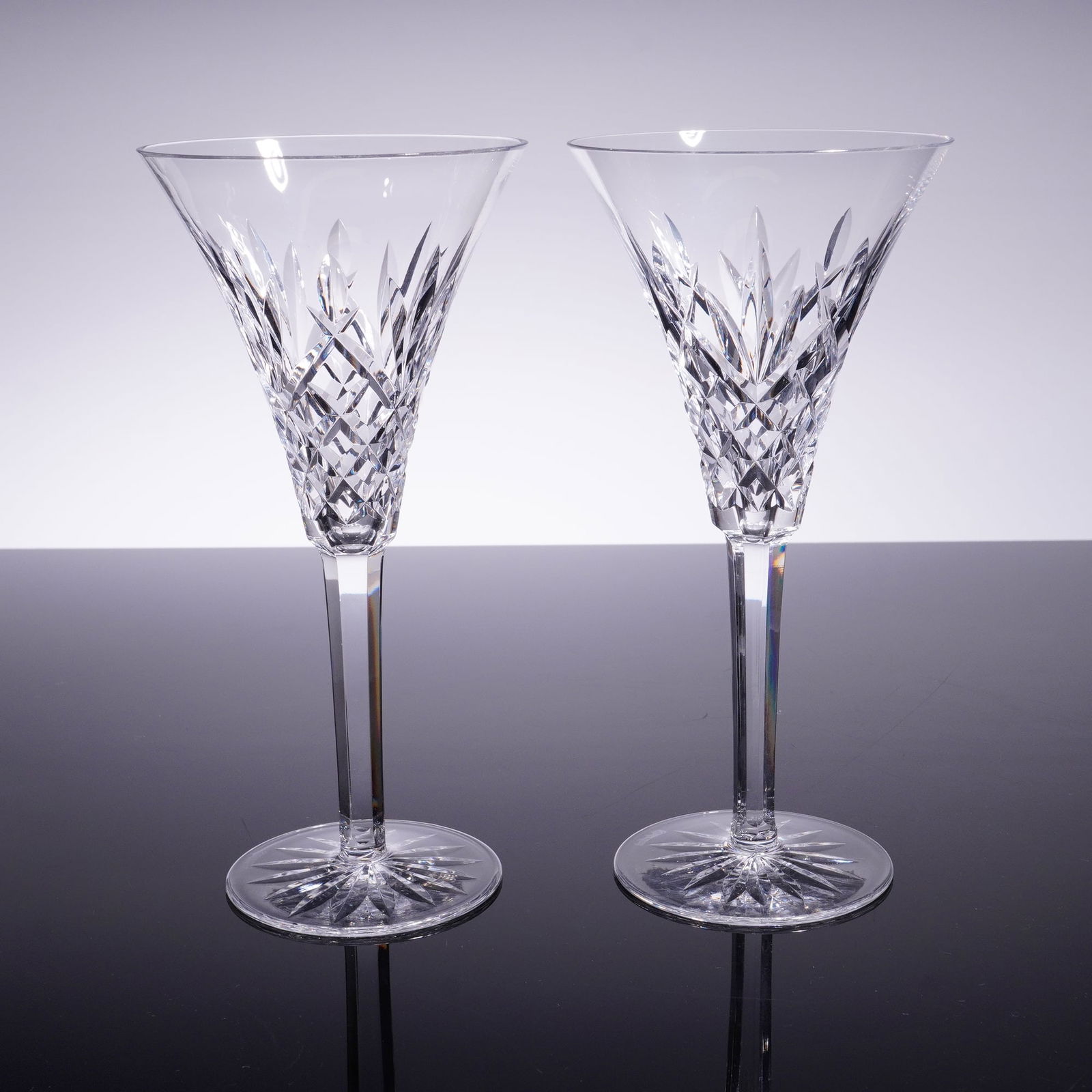 2pc Waterford Crystal Champagne Flutes, Ashbourne: A pair of clear crystal stemmed glasses, featuring a flared bowl deeply cut with a diamond and wedge lattice pattern intersected by vertical panels. The bowl rests on a tall, clear stem connected to a