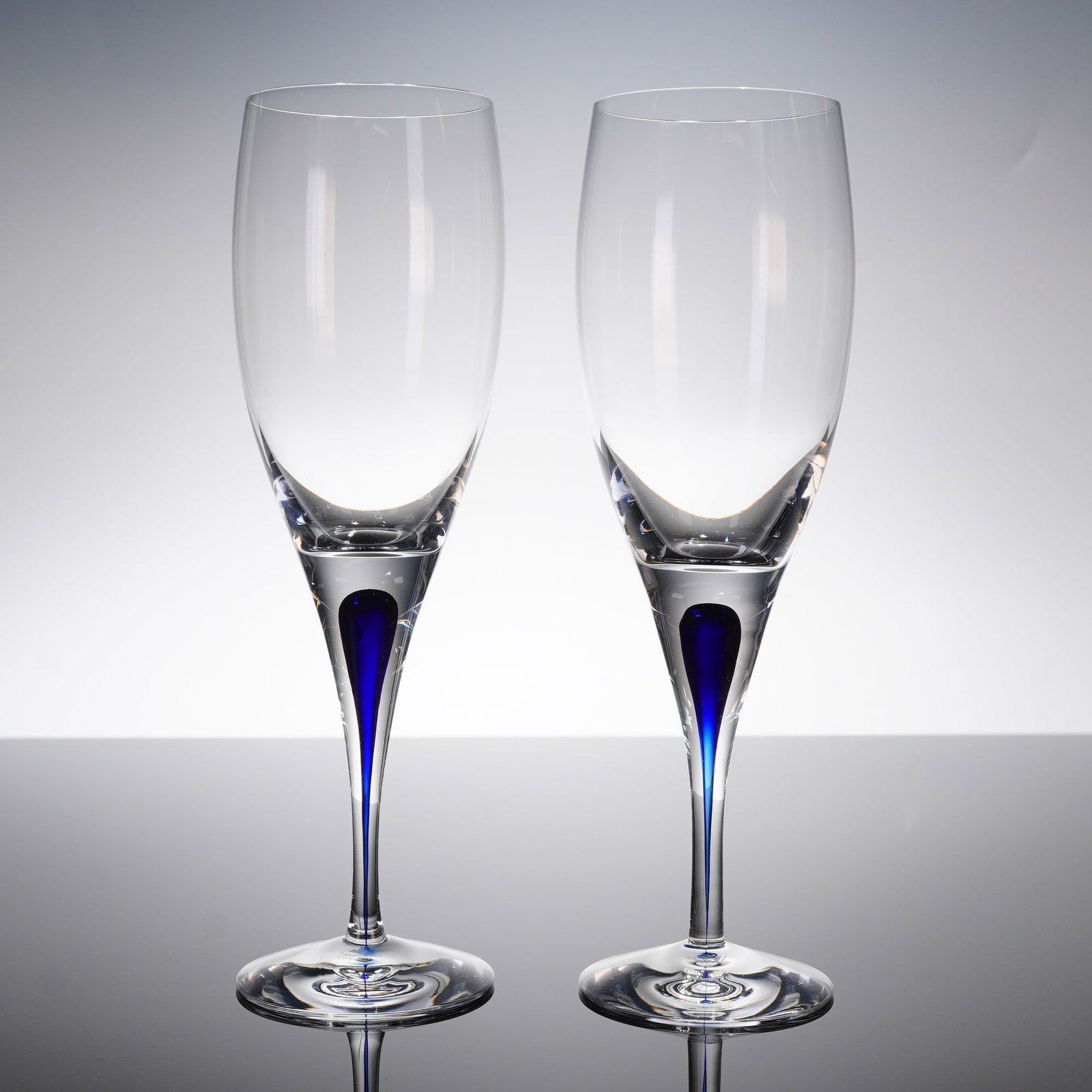 A Pair of Orrefors Intermezzo Blue Crystal Champagne Flutes: A pair of Orrefors Intermezzo Blue crystal glasses designed as champagne flutes, consistent with modern Swedish stemware. The 2pc set is executed in high-clarity lead crystal. Each fi?ute features a t