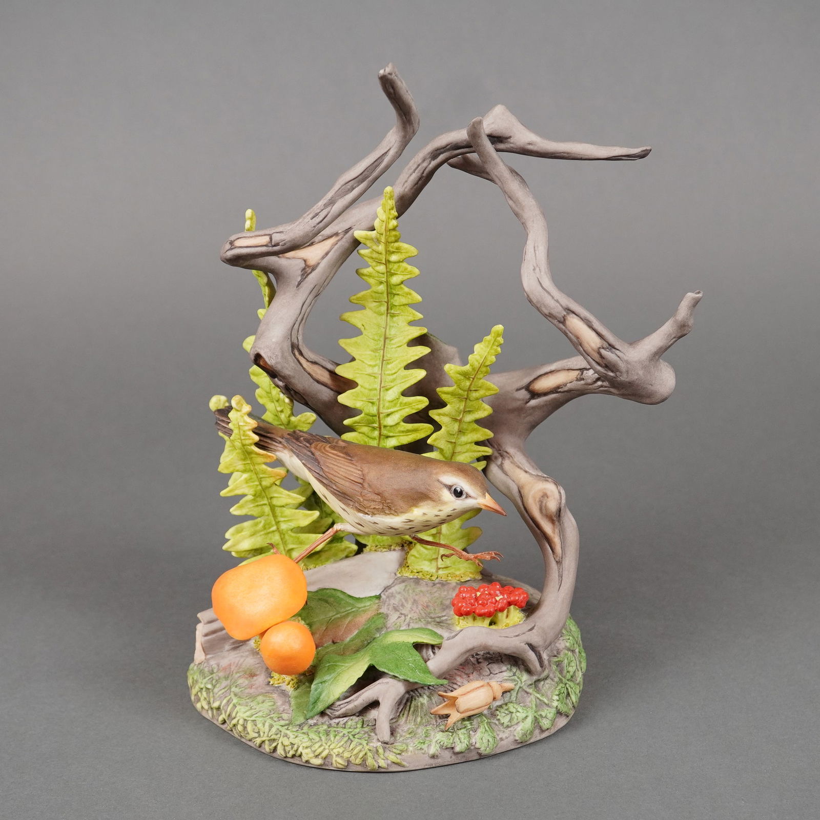 Boehm Porcelain Figurine, Northern Water Thrush 490: A single, hollow-cast porcelain sculpture by Boehm titled the Northern Water Thrush. The naturalistic piece depicts a small brown songbird perched amidst a detailed forest floor environment, featuring