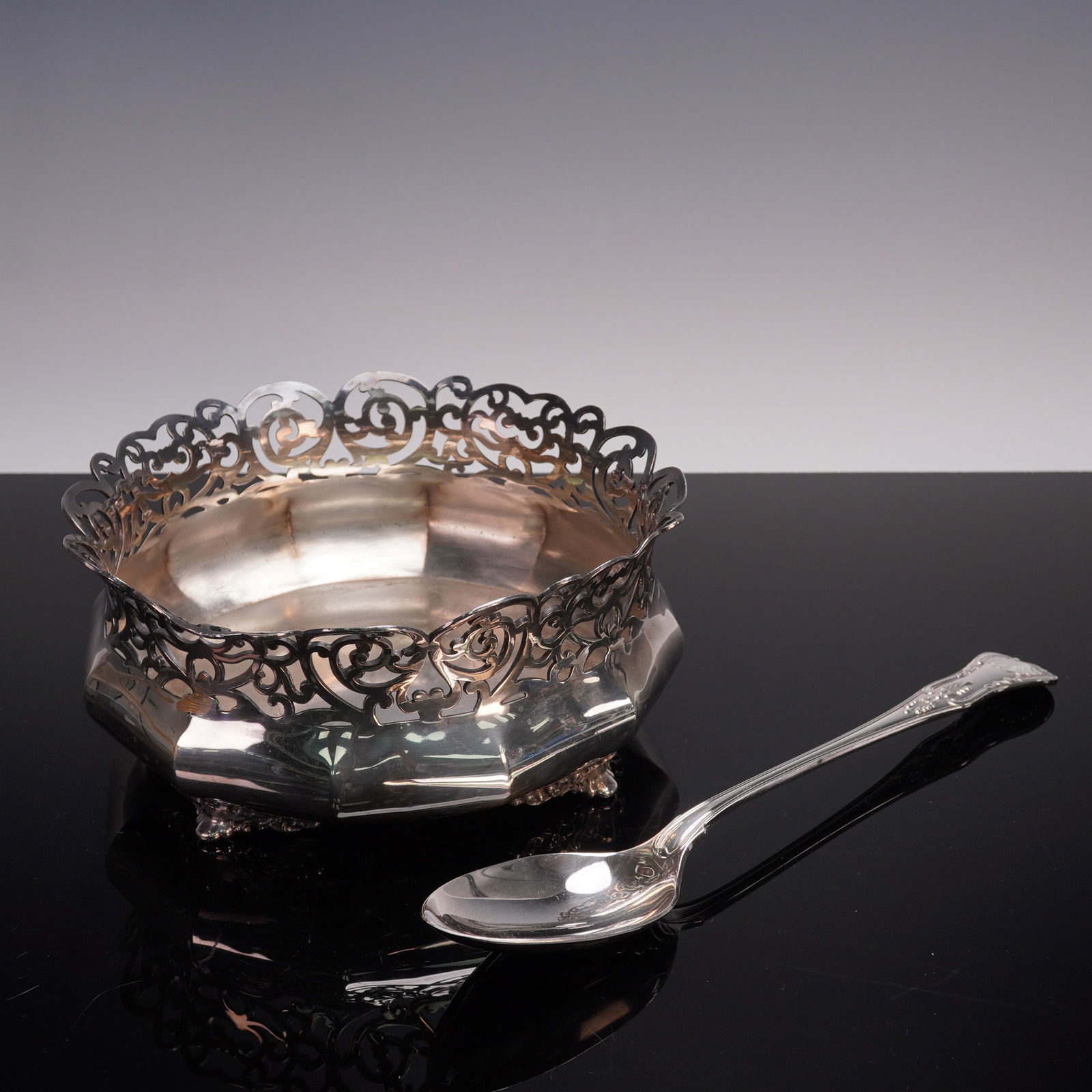 2pc Reed & Barton Silverplate Bowl and Serving Spoon: An elegant set featuring a bowl and serving spoon, the bowl of octagonal form raised on scrolling feet. The spoon's handle adorned with a shell and scroll work and the bowl with pierced border incorpo