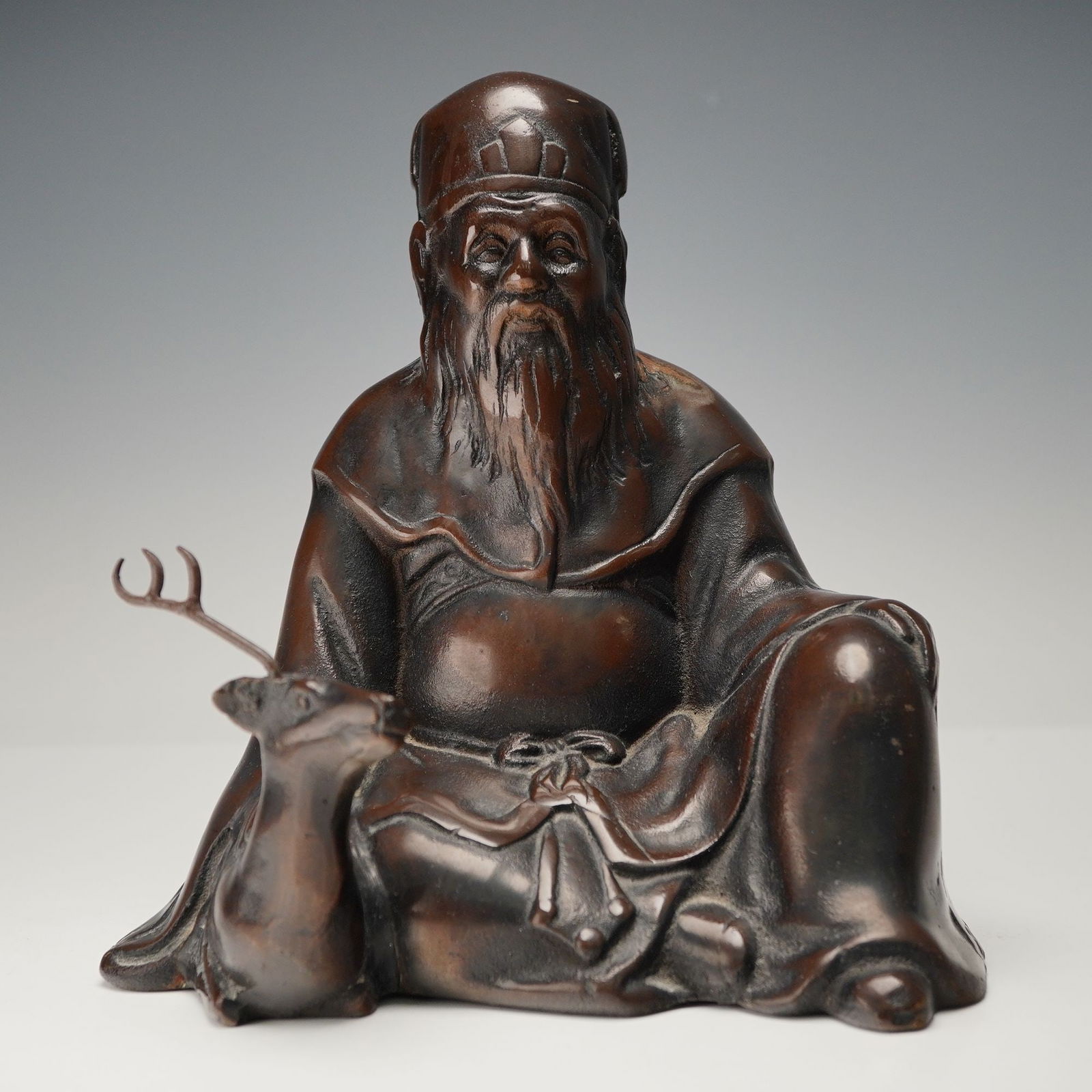 Shoulao and Deer Bronze Sculpture: Finely cast bronze sculpture depicting Shoulao, the Chinese god of longevity, seated with a gentle, wise expression beside his symbolic companion, the deer, representing immortality and prosperity. Th
