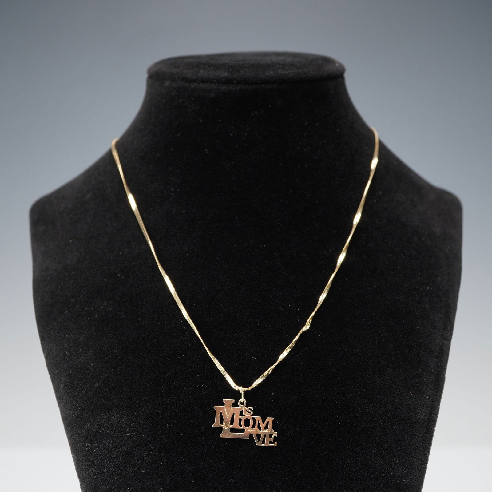 14K Gold Mom is Love Pendant Necklace: Composed of a flat twisted-link chain with a pendant formed in a block-letter arrangement reading "Mom is Love." The chain is marked 14KT near the clasp, and the pendant is stamped 14K on the reverse.