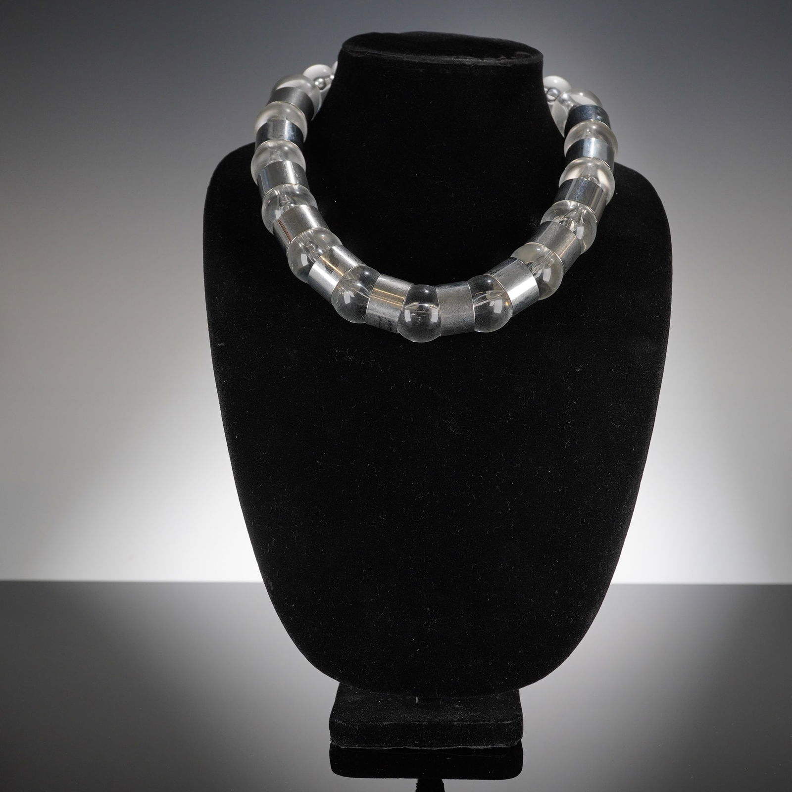 Modernist Clear Bead and Silver-Tone Spacer Necklace: A modernist necklace featuring a bold, chunky design. The piece is constructed of 12 large, clear components, appearing to be glass or acrylic, alternating with 11 smaller, highly reflective silver-to