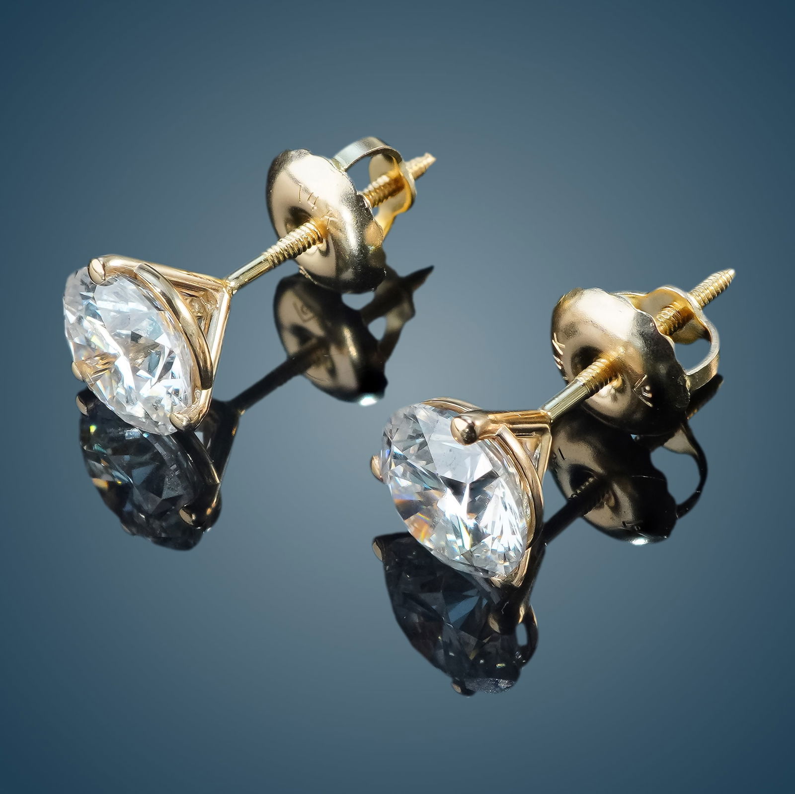 Pair of 14K Gold and 1.50ctw Diamond Stud Earrings: A pair of 14K yellow gold earrings featuring a three-prong martini setting and screw-back design. Each prong holds a round cut diamond with E color grade and VS1 clarity. The diamonds have a combined