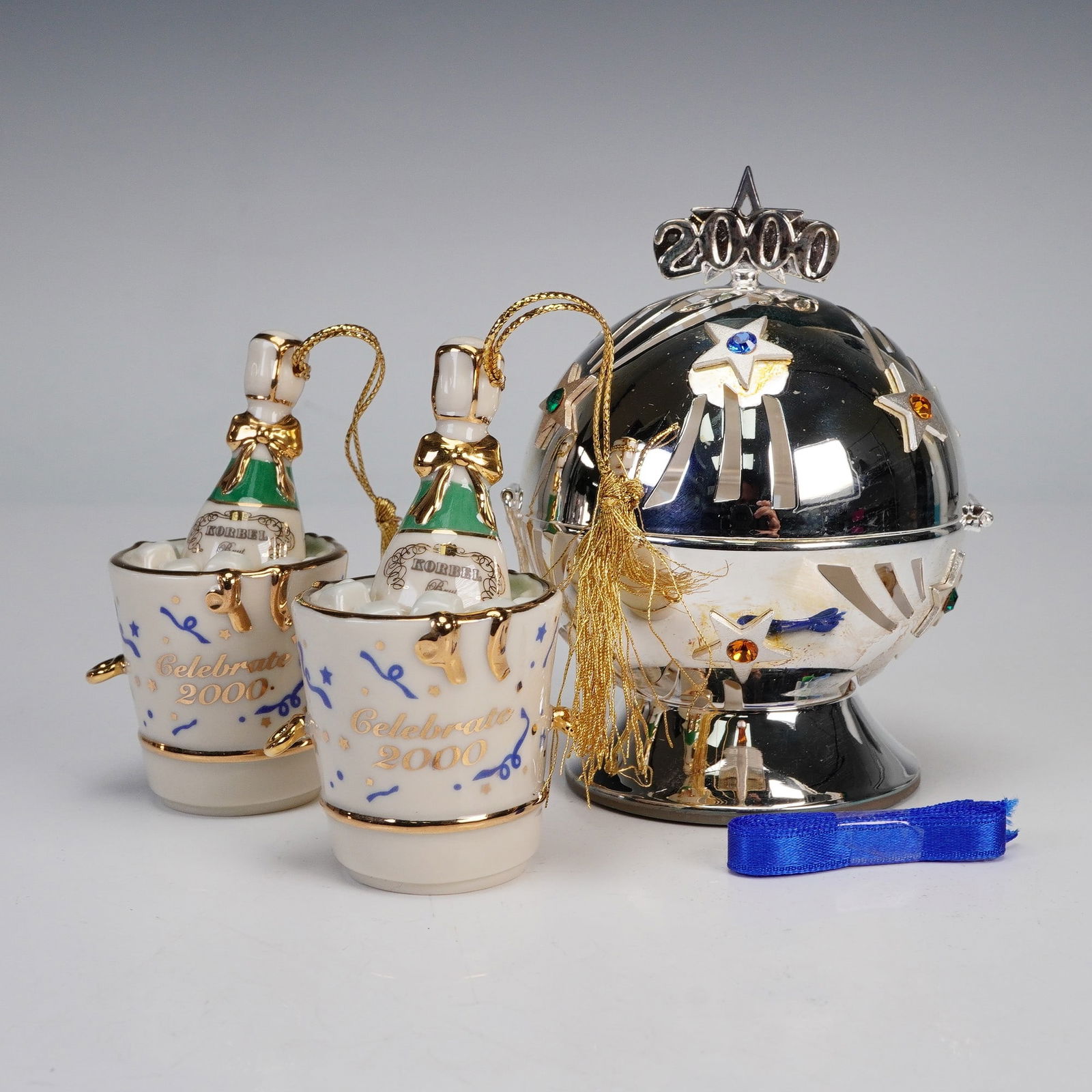 3pc Lenox Celebrate 2000 Millennium Ornaments: Lenox Celebrate 2000 Millennium collection ornaments, including two porcelain champagne bucket ornaments with gold accents and one silver ball ornament. The ball ornament features cutout star designs