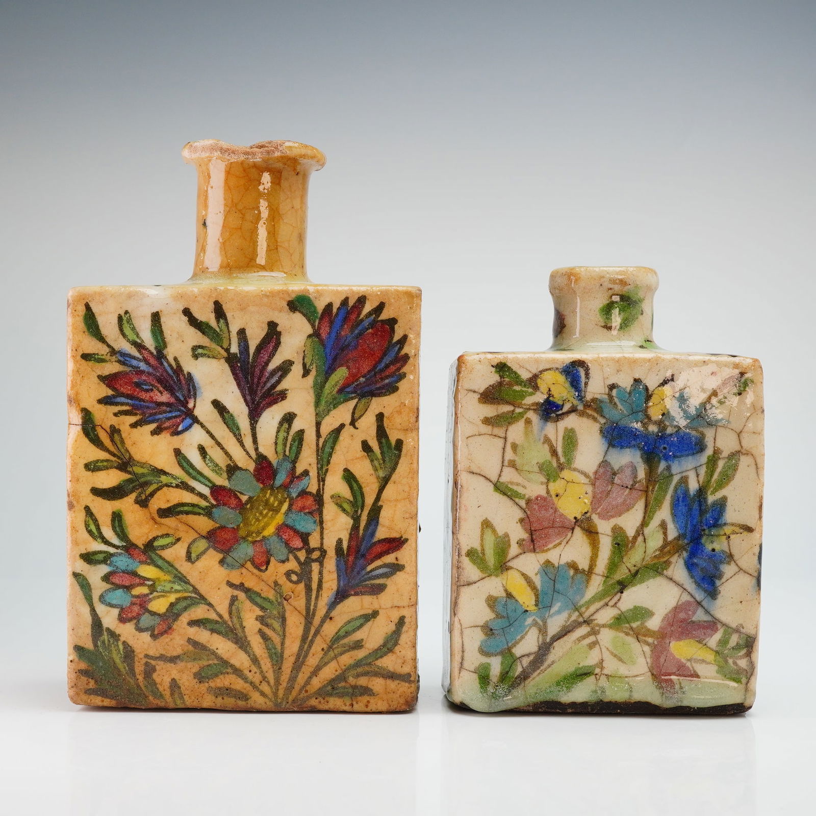 2pc Antique Persian Qajar Iznik Pottery Bottles, Branch & Leaf Design: Two antique Persian pottery bottles, attributed to the Qajar period and decorated in the Iznik-inspired branch and leaf design. The pair comprises one larger, darker-toned bottle measuring approximate