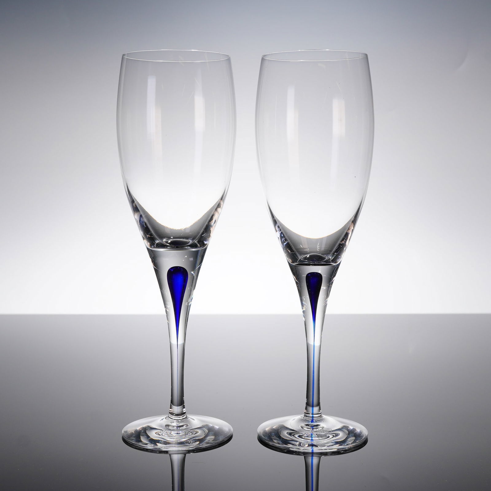 A Pair of Orrefors Intermezzo Blue Crystal Claret Wine Glasses: A pair of modern crystal stemware pieces, identified as the Intermezzo Blue patern, designed by Erika Lagerbielke for Orrefors, Sweden. The pieces are constructed of clear colorless crystal, featuring
