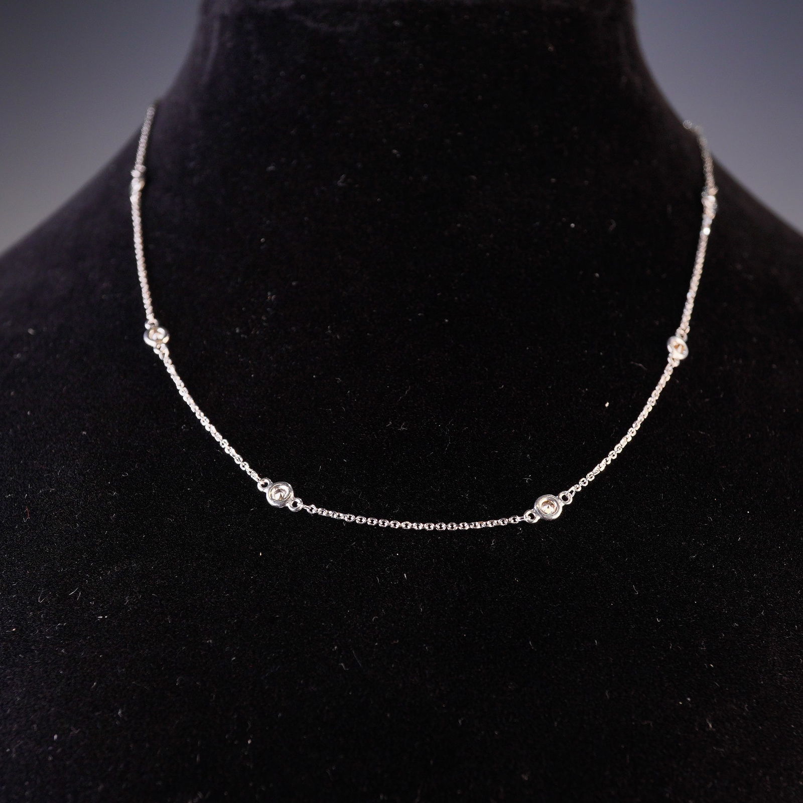 14K White Gold and 0.50ctw Diamond Bezel Set Station Necklace: A contemporary station-style necklace featuring nine round brilliant-cut diamonds. Each stone is housed in a white gold bezel setting, spaced at intervals along a fine 14K white gold cable chain. The