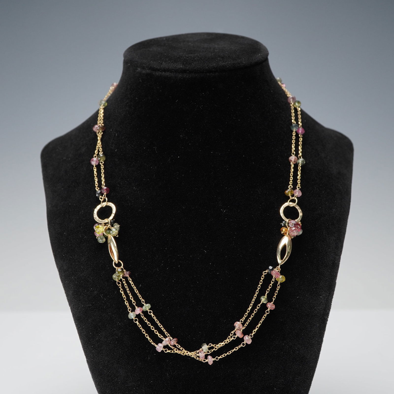 14K Gold Multi-Color Tourmaline Bead Necklace: Adorned with faceted tourmaline beads in hues of pink, green, yellow, and smoky brown, this 14K gold necklace showcases a three-strand draped design joined by polished oval and hammered rings. Each be