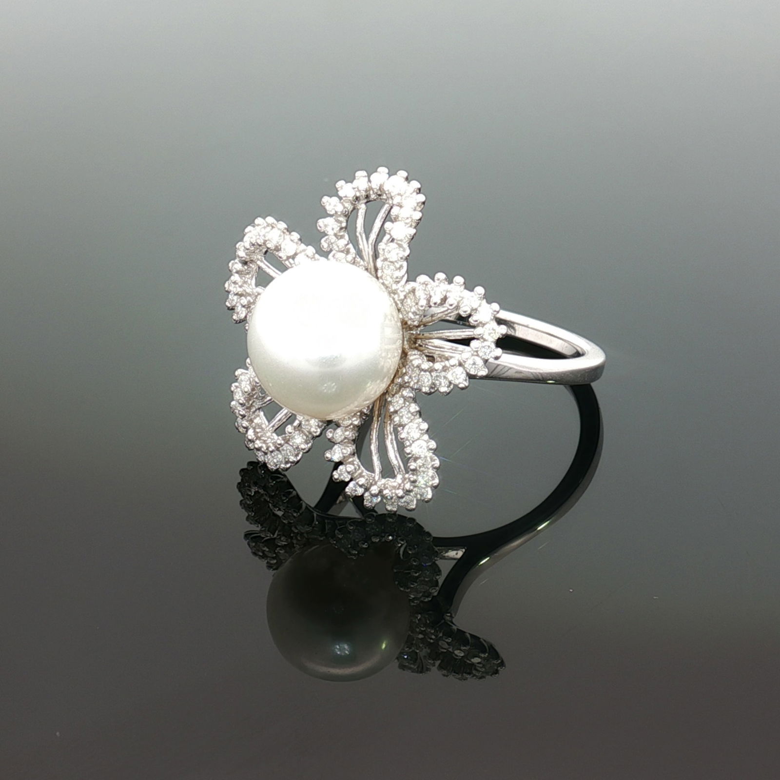 Estate 18K White Gold South Sea Pearl and Diamond Ring: An estate cocktail ring featuring a prominent round white South Sea pearl centerpiece framed by a five-petaled floral motif crafted in polished 18K white gold. Each petal features an open-work design