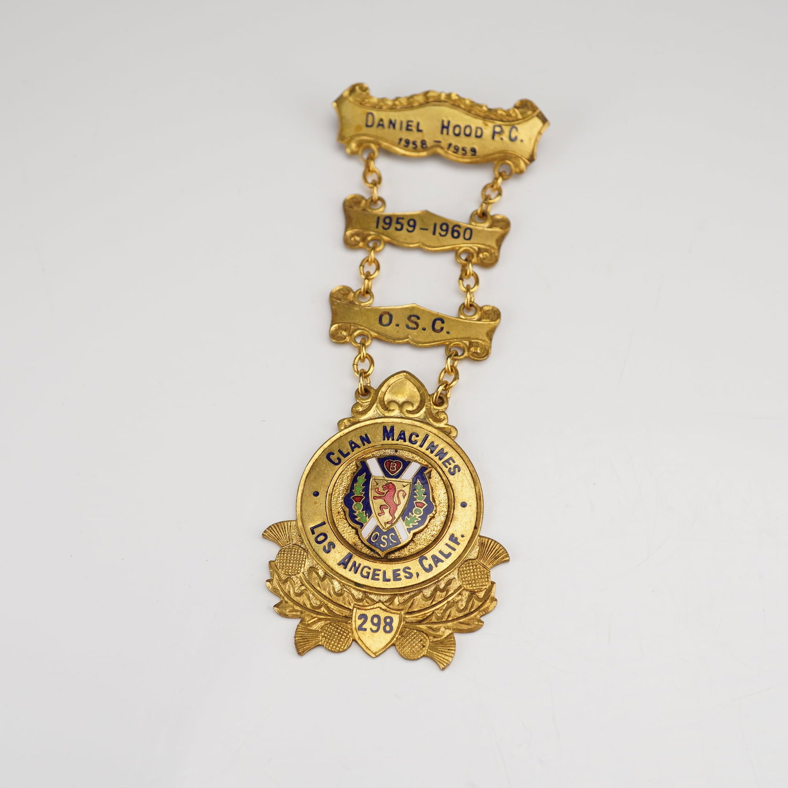 Mid-20th Century Clan MacInnes Los Angeles Fraternal Presentation Badge: A single mid-20th century fraternal or societal presentation badge constructed from gold-toned base metal and featuring multicolor enamel accents. The regalia is designed with four linked components: