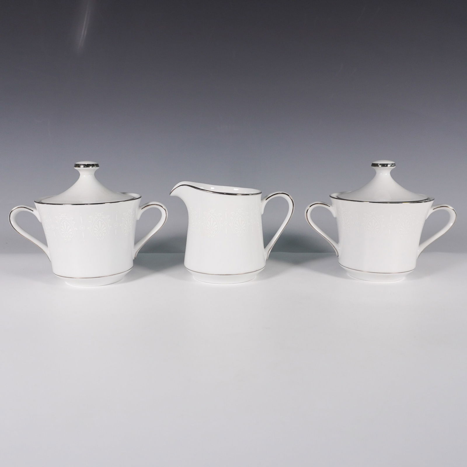 3pc Crown Empire Fine China Sugar Bowls and Creamer, Princess: Crown Empire fine china tableware set in the Princess pattern, featuring white floral and fleur-de-lis decorations with metallic-silver trim. This collection includes two covered sugar bowls and one c