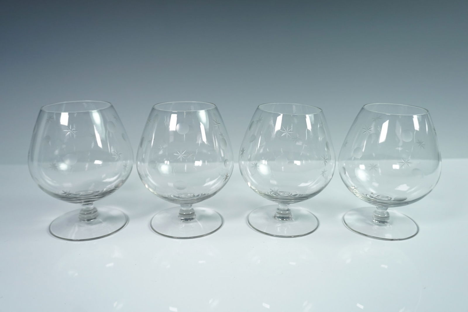 4pc Star and Dot Etched Brandy Glasses: Set of four clear glass brandy snifters, each featuring a rounded bowl, short stem, and broad footed base. The glasses are decorated with an etched pattern of stars and dots evenly spaced around the b