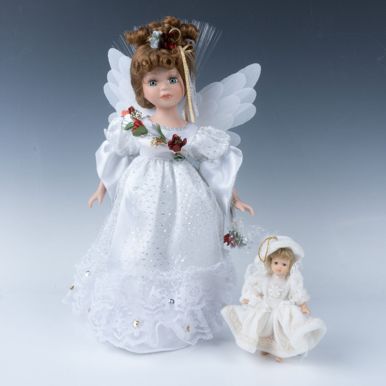 2pc Holiday Porcelain Doll & Ornament: Lot includes small porcelain, hand painted doll ornament dressed in winter white and battery-operated fiber optic angel dressed in white satin gown with red holly floral accents with display stand. La
