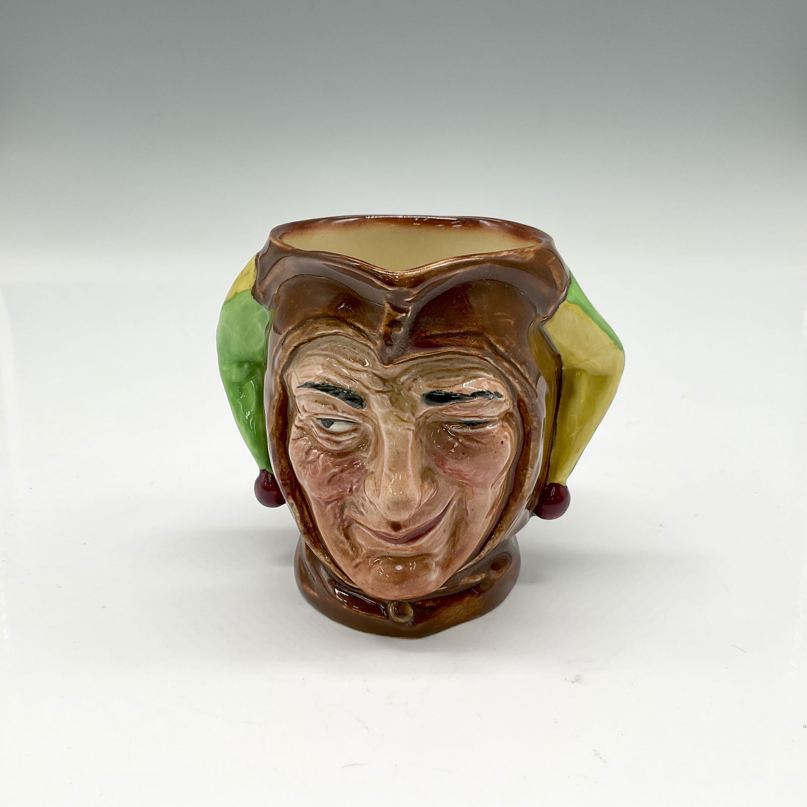 Jester D5556 - Small - Royal Doulton Character Jug: Brown, green and yellow coloration. Royal Doulton backstamp. Artist: Charles J. Noke Issued: 1936 - 1960 Dimensions: 3.25"H Country of Origin: England