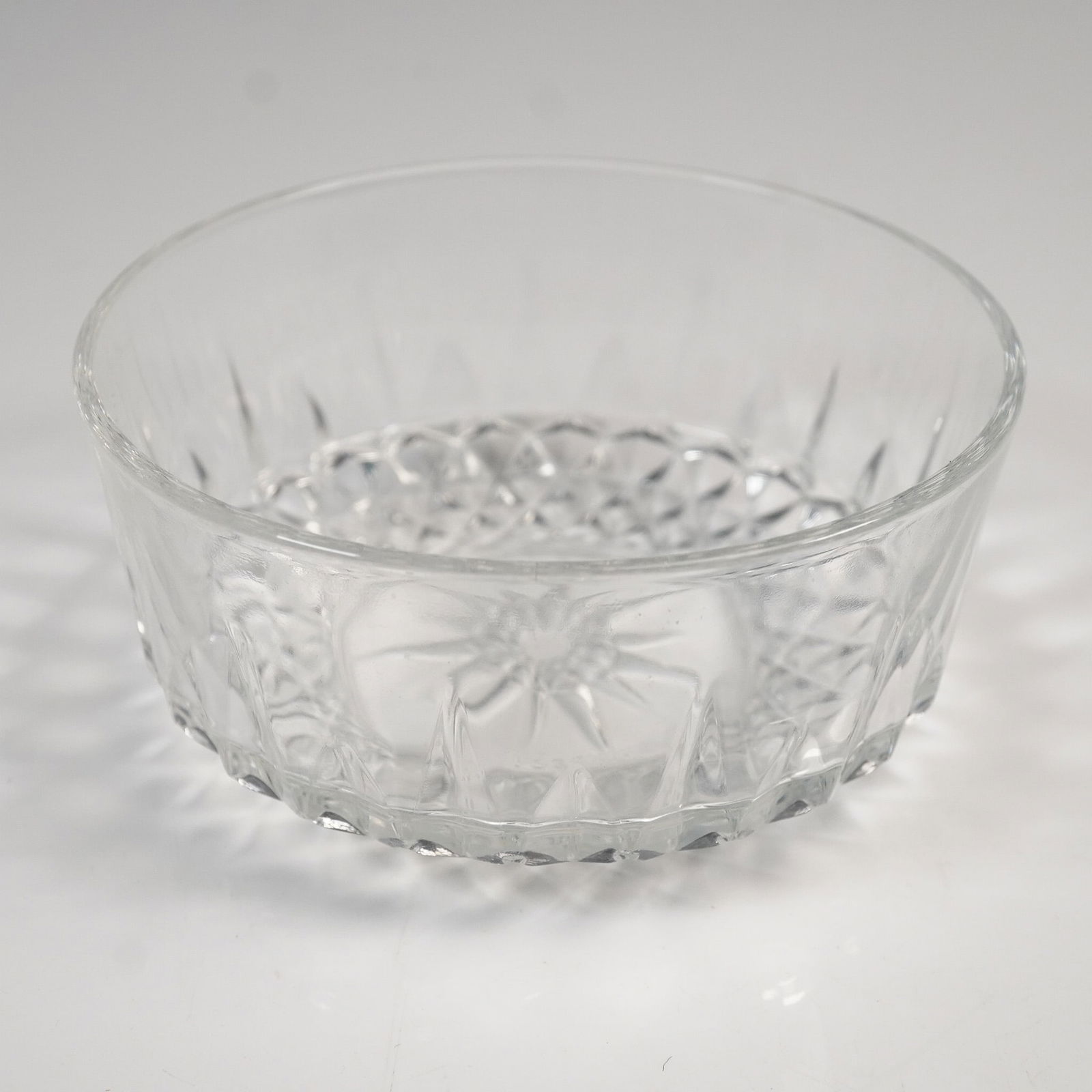 Vintage Arcoroc France Glass Bowl: A clear glass bowl featuring vertical cut motifs along the walls and a diamond cut pattern around the base. The bottom displays a sunburst star design. The bowl is marked 'Arcoroc France' on the under