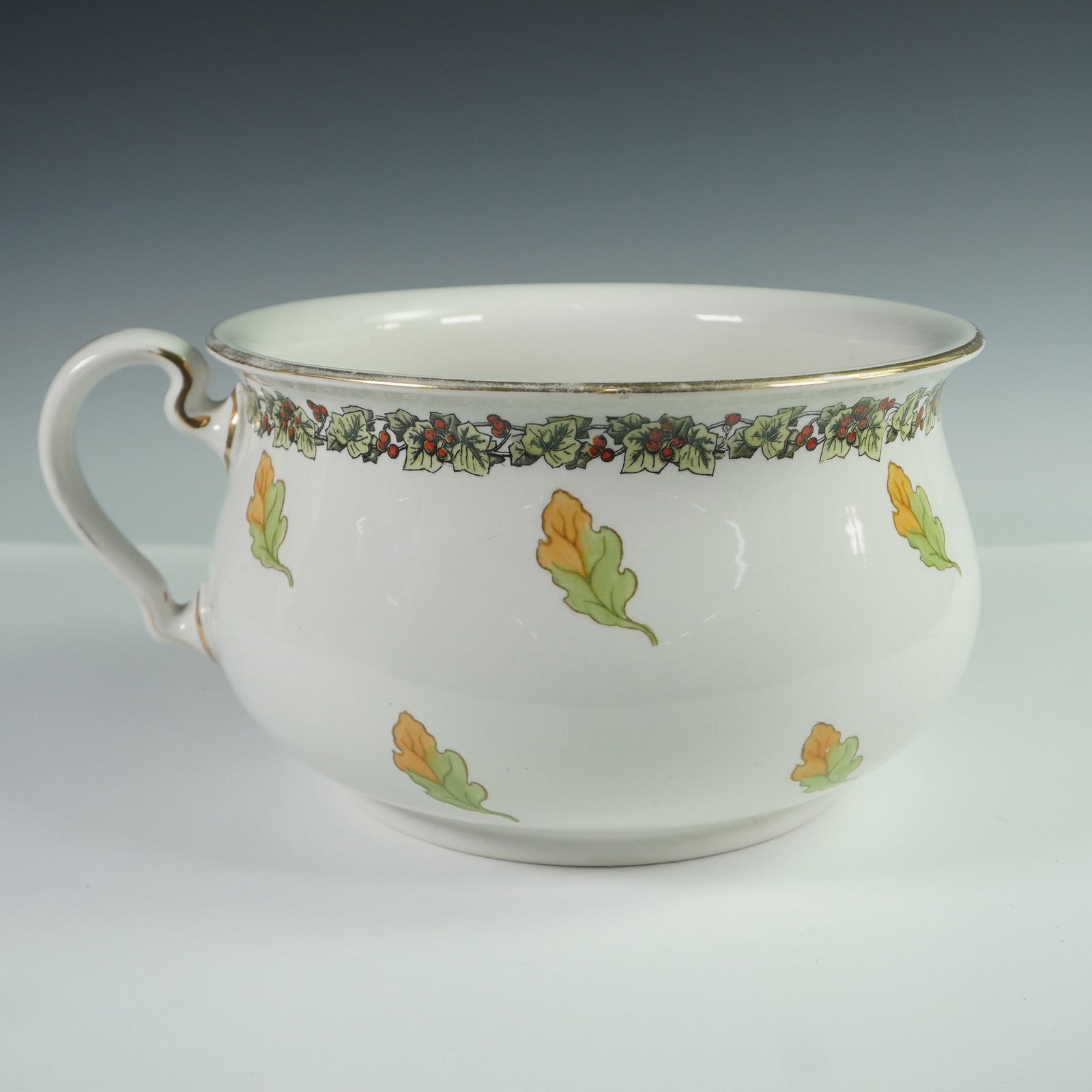 Bisto England Ceramic Chamber Pot, Oak Leaf and Holly Motif: A vintage ceramic chamber pot by Bisto, England, featuring an autumnal oak leaf motif interspersed with a decorative holly and ivy garland around the rim. The piece has a classic form with a curled ha