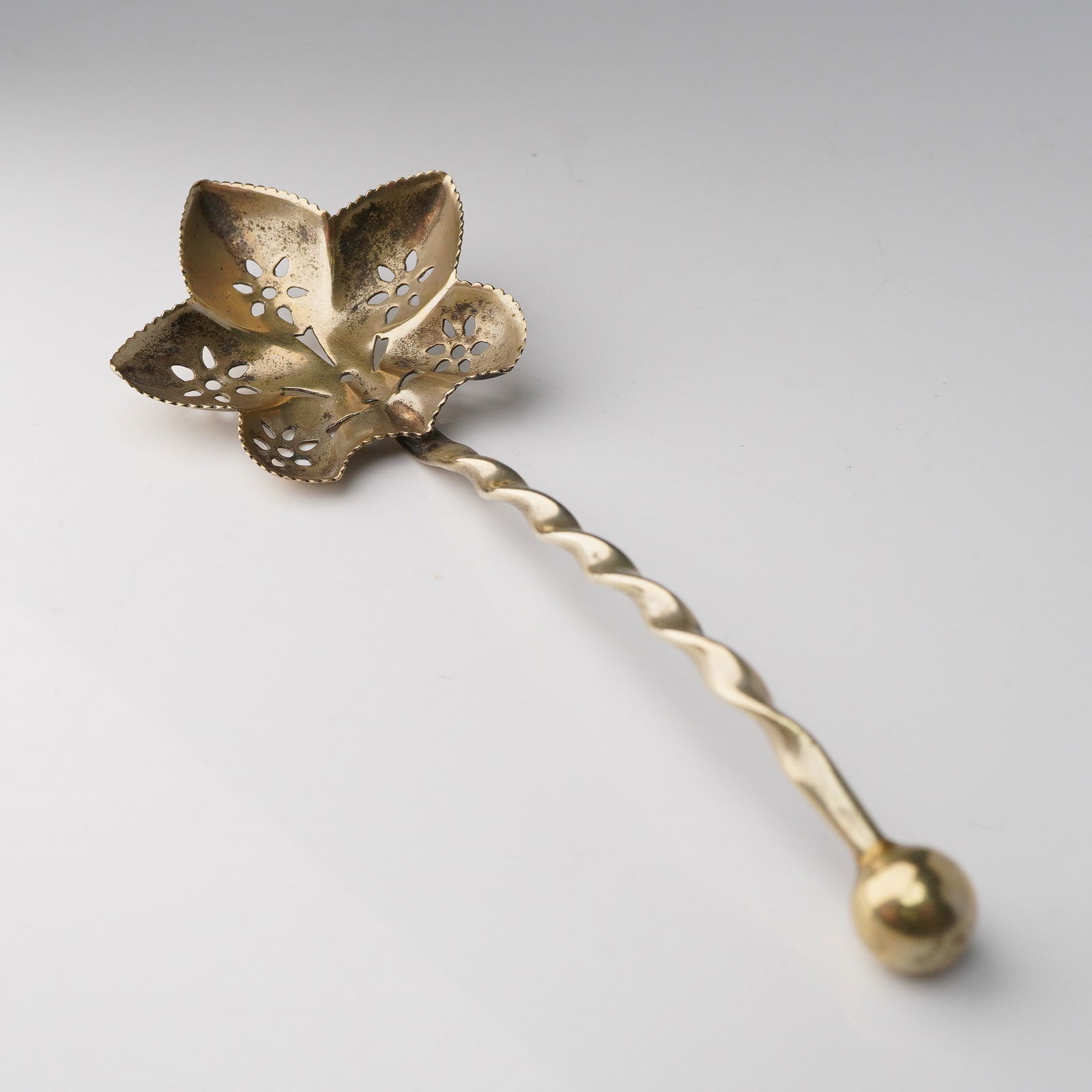 Vintage Pierced Leaf-Form Gilt Spoon with Twisted Handle: This unique vintage spoon features a finely detailed, leaf-shaped bowl with pierced floral accents and scalloped edges. The bowl's five-lobed form resembles a stylized vine or ivy leaf, adding decorat