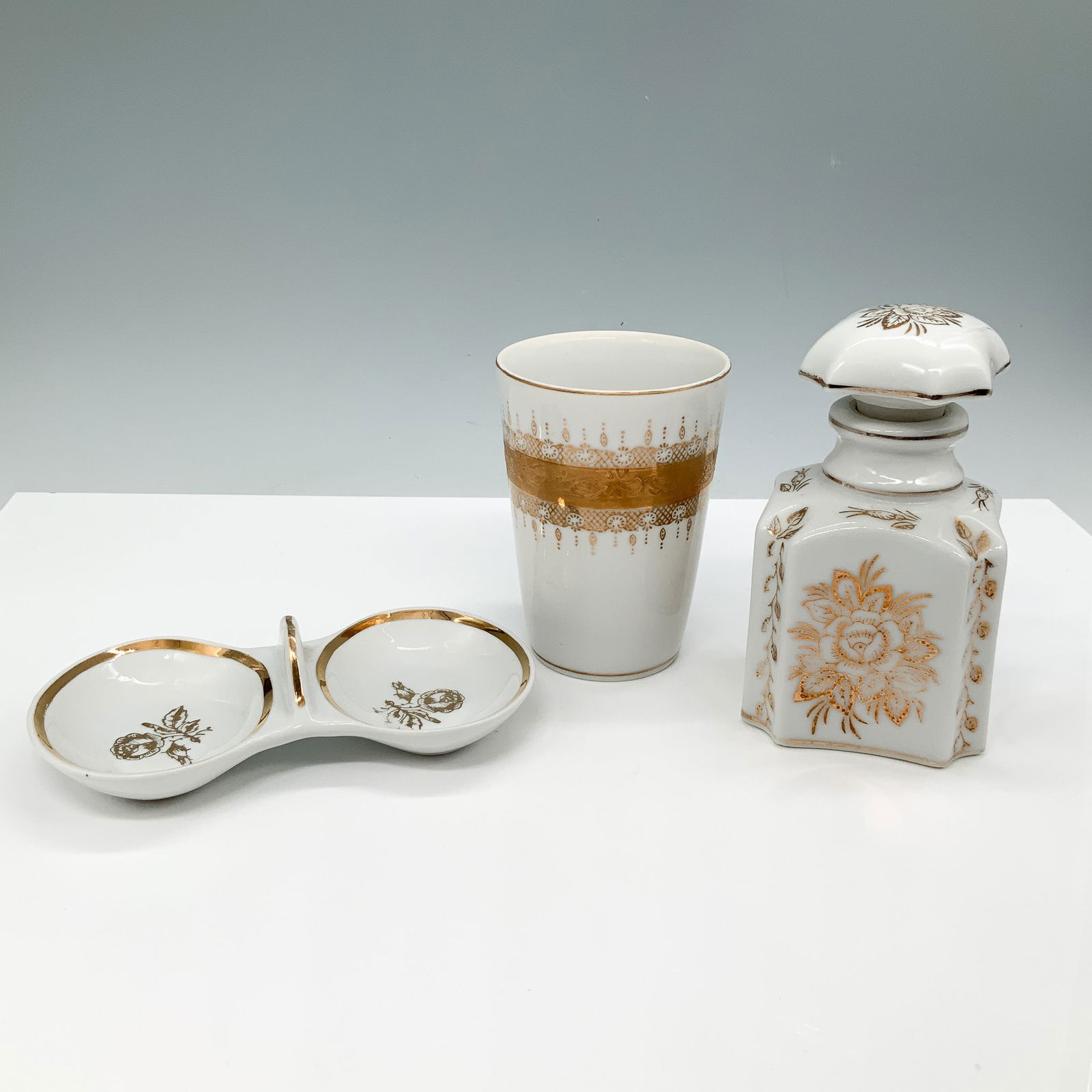 Decorative Floral Gilt Porcelain Vanity Set: A porcelain vanity set featuring gold accents, including a double dish with floral motifs and gilded trim, marked Jugoporcelain Titov Veles. The set also includes a decorative cup with an intricate go