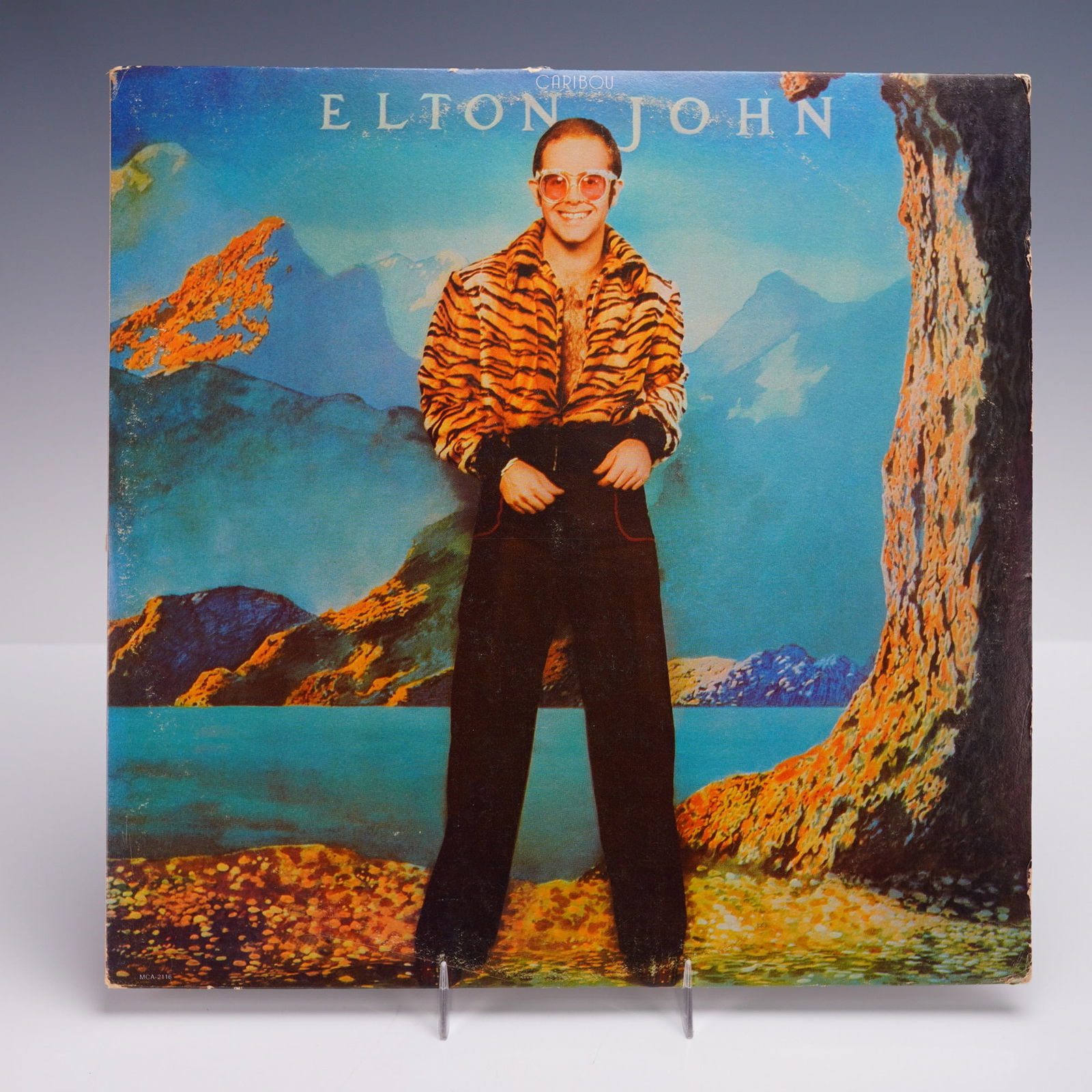 MCA Records Elton John Vinyl Record, Caribou: A 1974 U.S. pressing of Elton John's "Caribou" LP vinyl album, issued by MCA Records. The vividly stylized cover features a boldly attired Elton John standing against a surreal alpine landscape, with