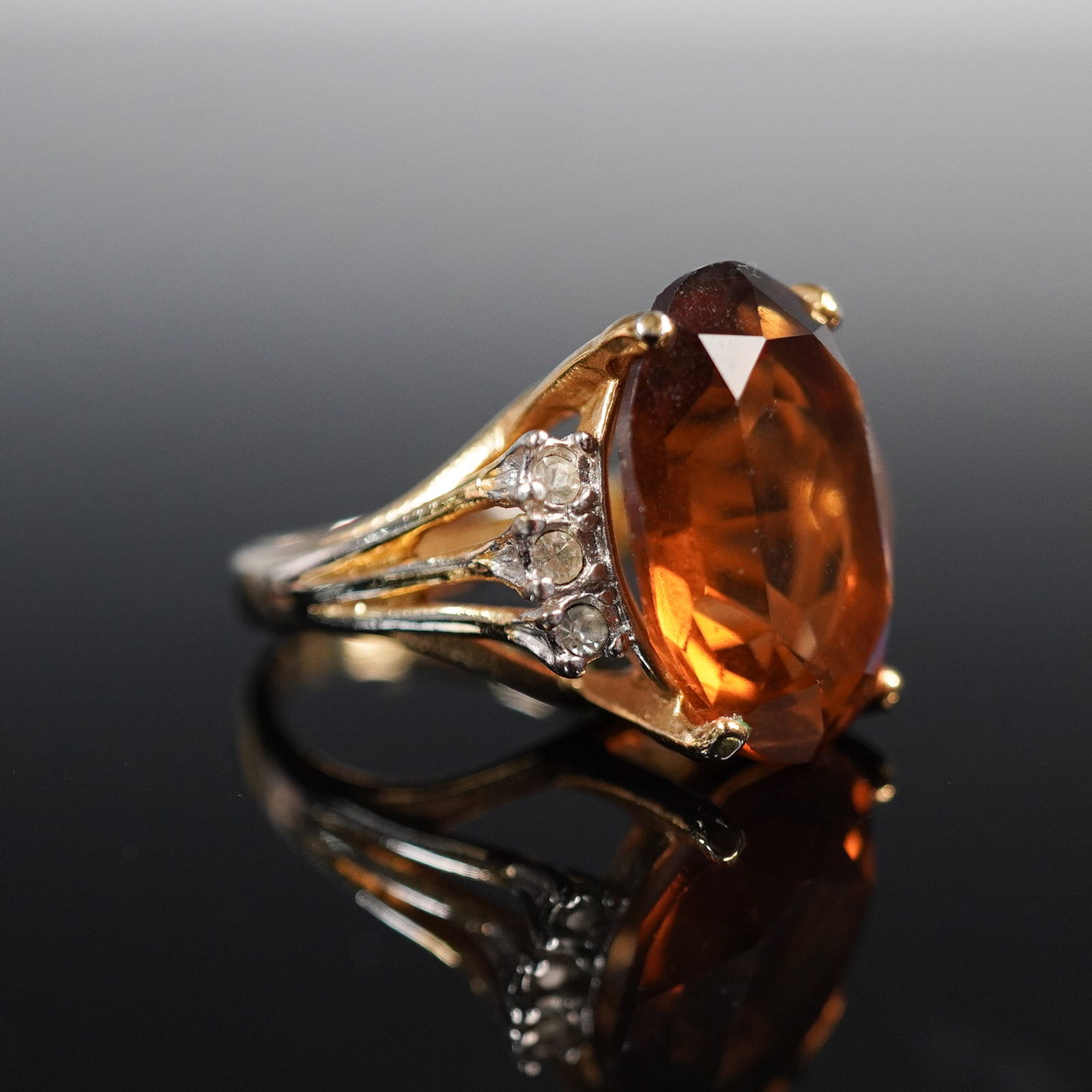 18K Heavy Gold Electroplated Cocktail Ring with Stone: A timeless 18K HGE cocktail ring featuring a large oval faceted citrine-colored stone, flanked by clusters of clear simulated diamond accents. This striking design captures classic glamour with a bold
