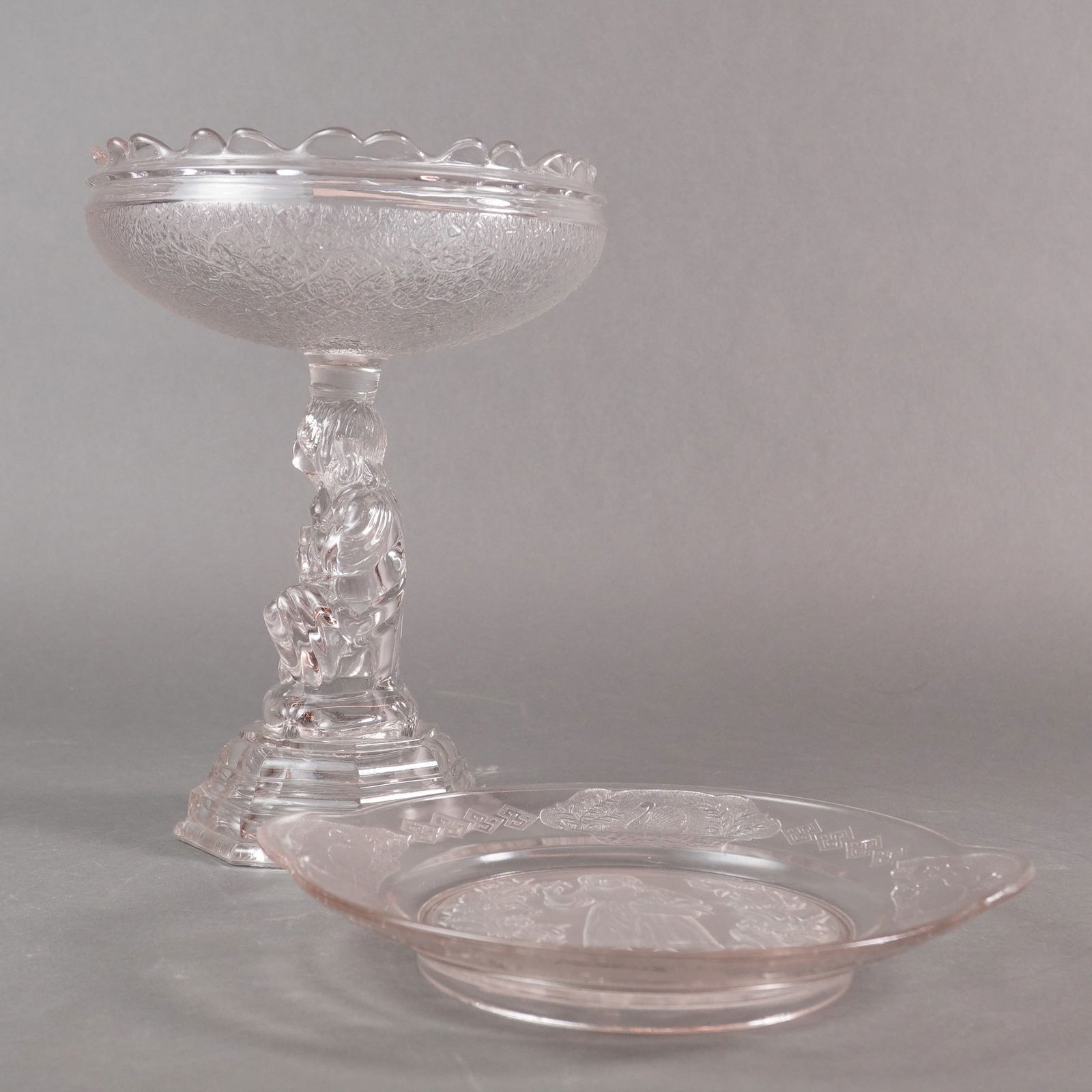 A Two-Piece Lot of EAPG Hobbs Brockunier Compote and Handled Plate: A two-piece lot of Early American Pressed Glass (EAPG) tableware rendered in a pale pink or blush amethyst hue. The collection includes a pedestal compote and a handled decorative plate. The compote i