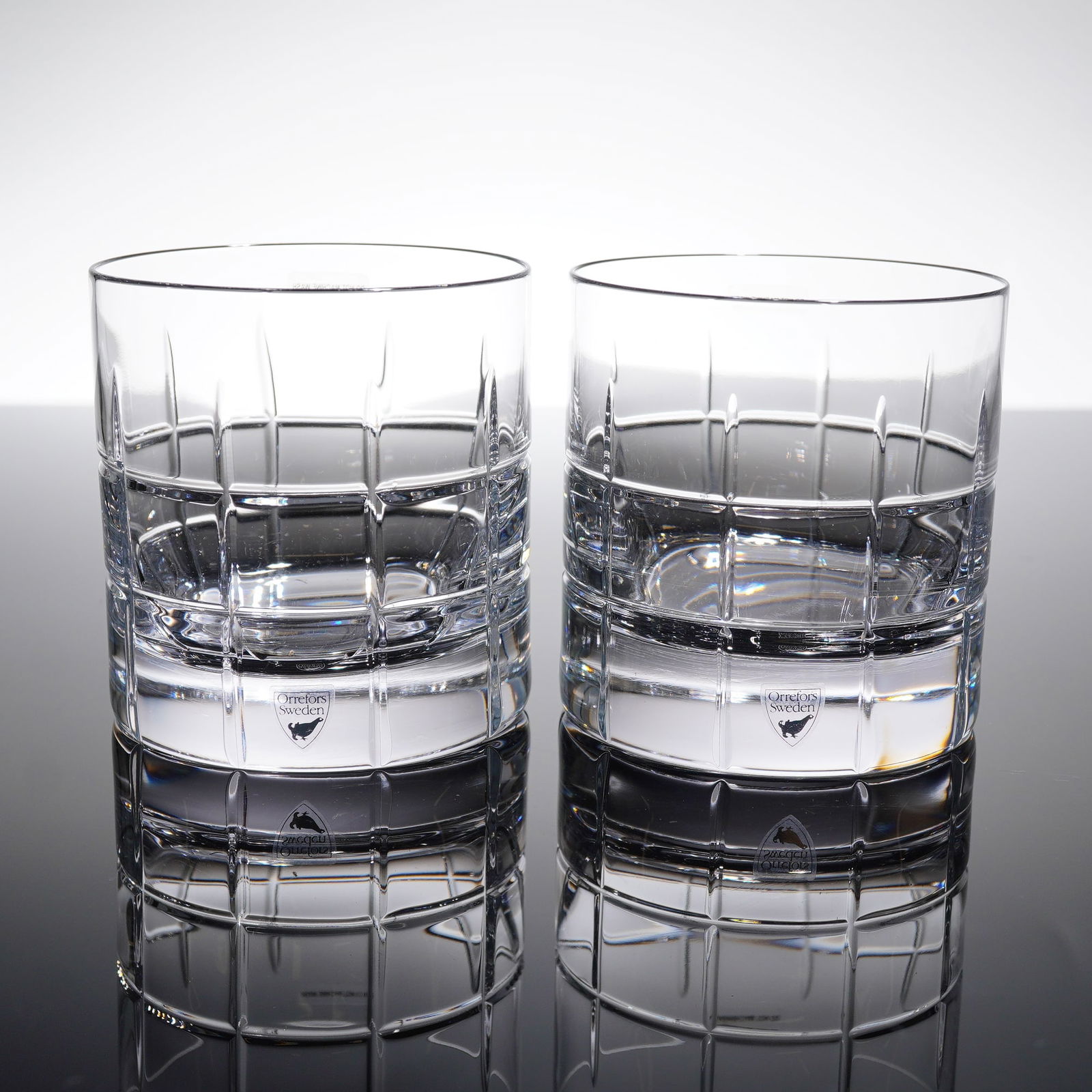 A Pair of Orrefors Crystal Double Old Fashioned Glasses by Jan Johansson: A two piece set of old fashioned whiskey tumblers, designed in the Street patern by Jan Johansson. Each glass is decorated with deep vertical and horizontal facets, creating a distinct geometric grid