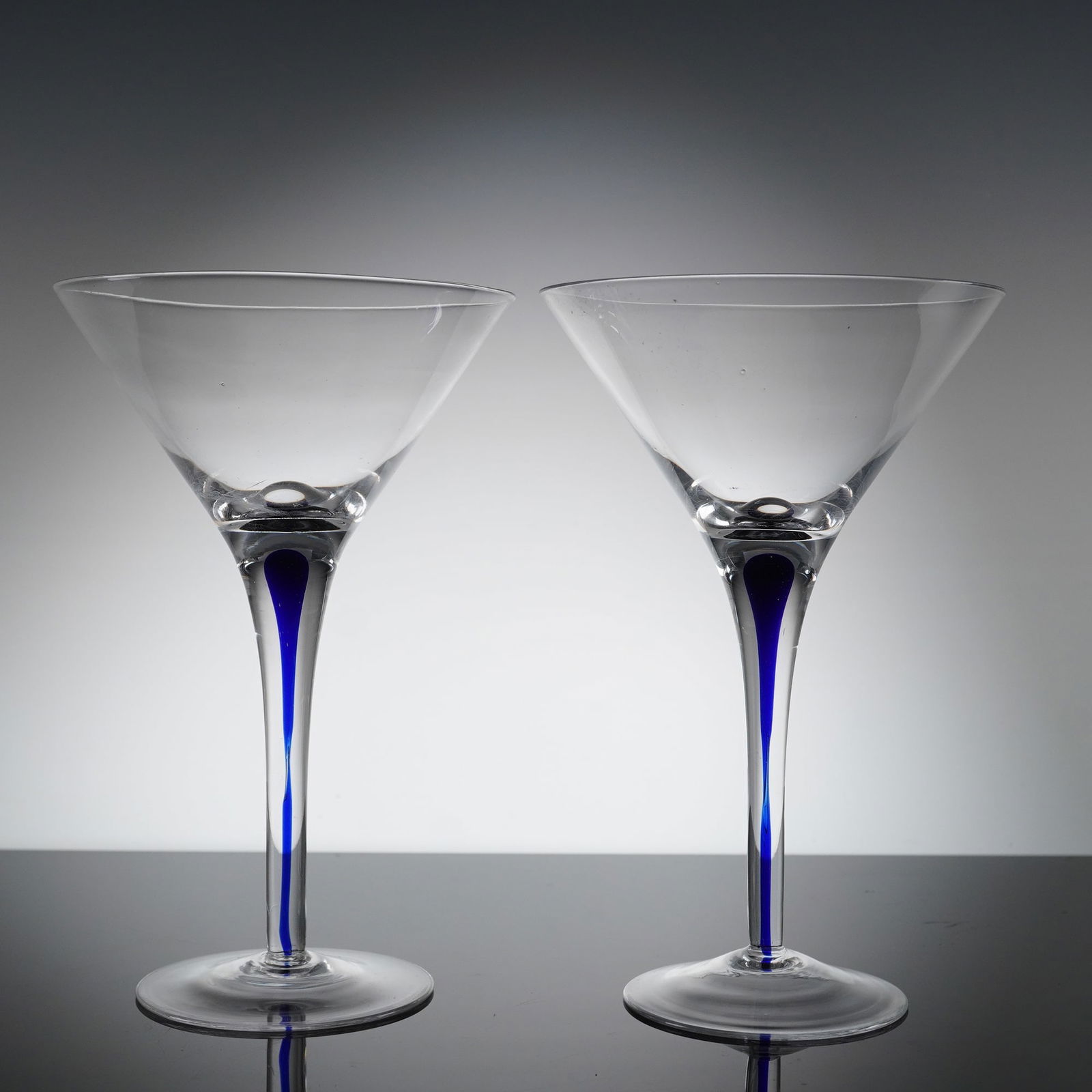 A Pair of Orrefors Intermezzo Blue Martini Glasses: This is a pair of contemporary martini or cocktail glasses atributed to the Orrefors Intermezzo Blue line. Each glass is constructed from clear colorless crystal glass, featuring a wide, inverted coni