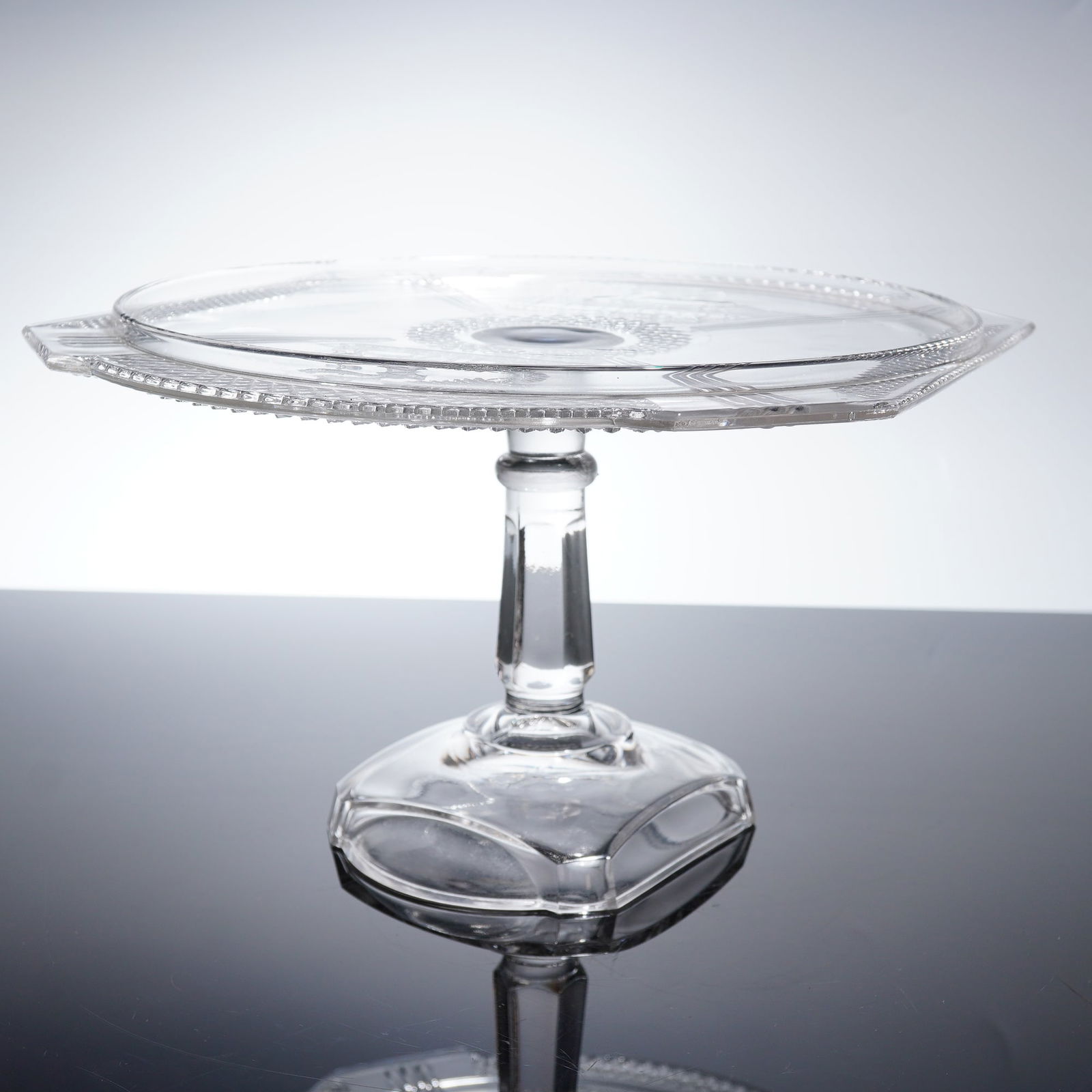 McKee & Brothers EAPG Pedestal Cake Stand, Deer and Pine Tree: 19th century McKee & Brothers cake stand that features a high, multi-faceted stem rising from a stepped, octagonal base. The platter is multi-sided and heavily decorated with pressed glass motifs. The