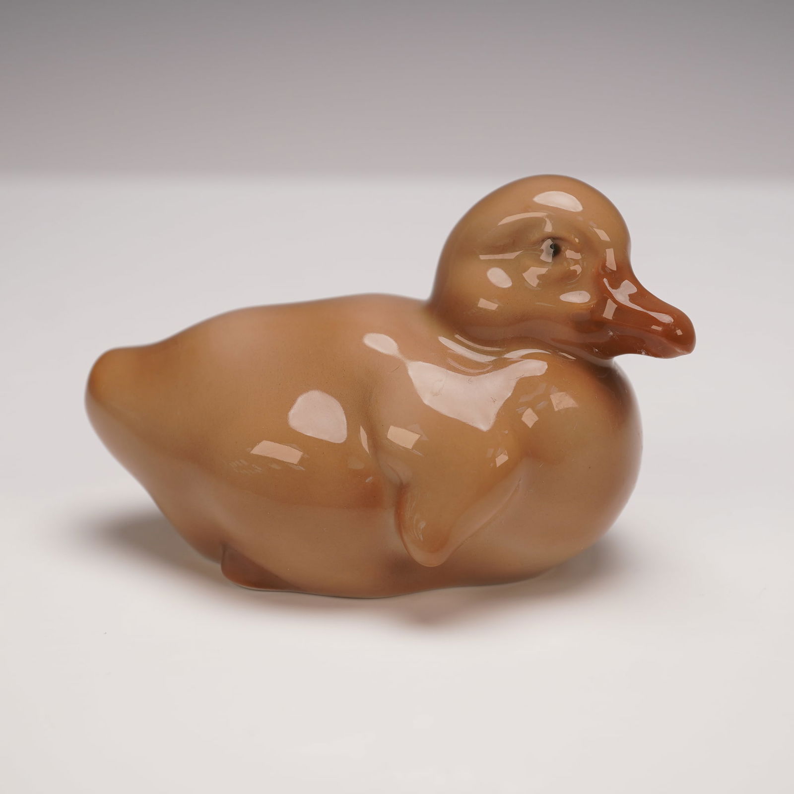 Bing & Grondahl Porcelain Duckling Figurine, 1548: This charming porcelain duckling figurine was crafted by Bing & Grondahl of Denmark, known for their exceptional quality and artistry. Finished in a warm brown glaze, the piece captures the gentle, ro