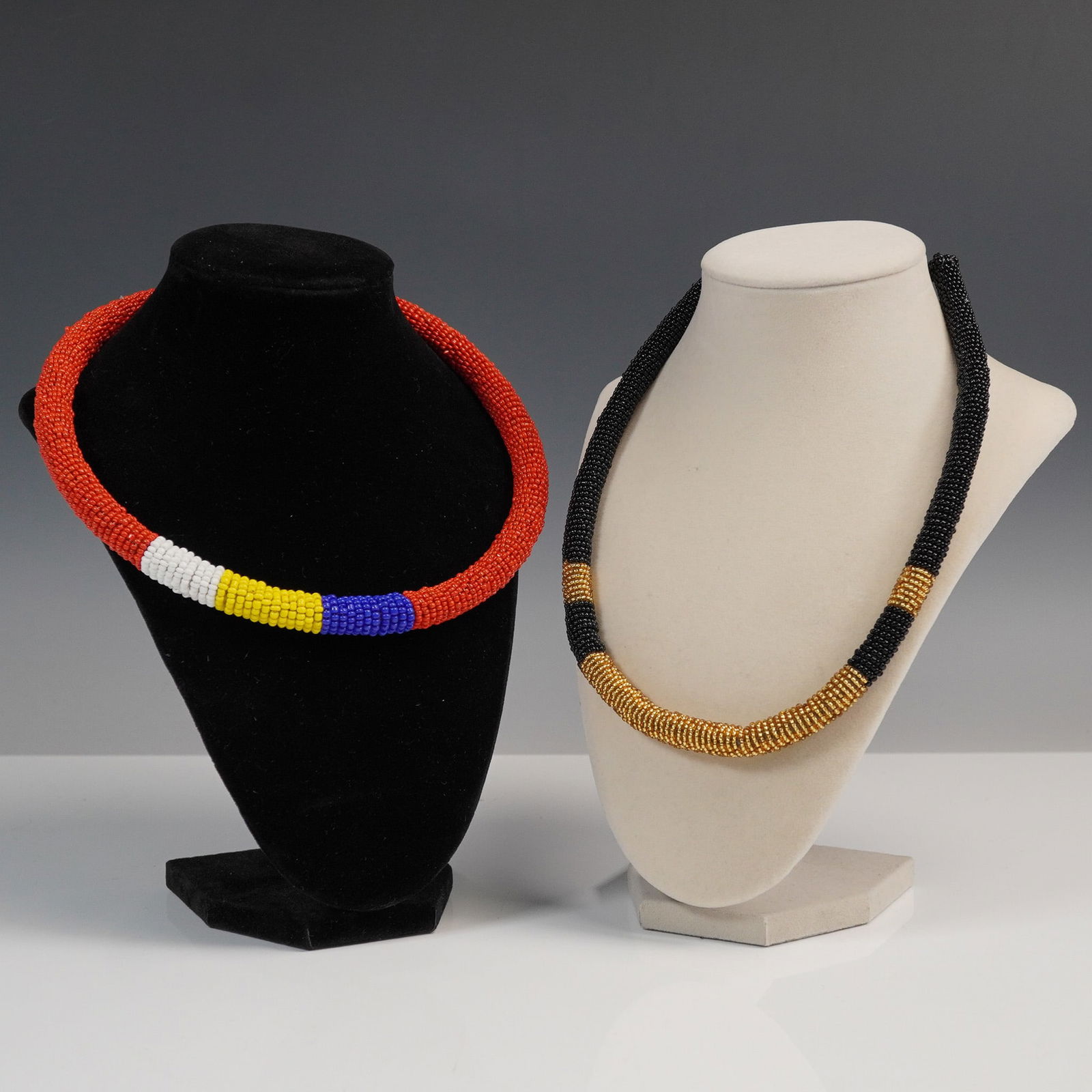 2pc Hand Beaded Rope Necklace Set: Pair of delightful hand beaded rope necklaces featuring intricate beadwork in bold color combinations. One necklace showcases a vibrant mix of red, white, yellow, and blue beads in a tubular design wi