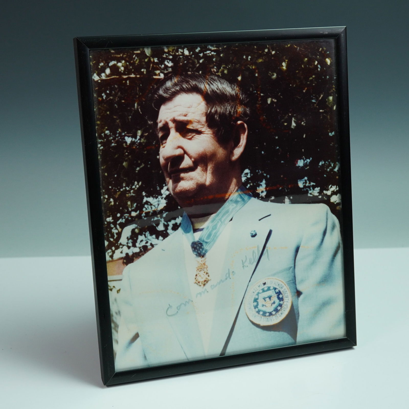 Charles Commando Kelly Signed Medal of Honor Portrait Photo: Framed color portrait of World War II Medal of Honor recipient Charles "Commando" Kelly, signed "Commando Kelly" across his jacket. Kelly is shown wearing his Medal of Honor and a blazer patch reading