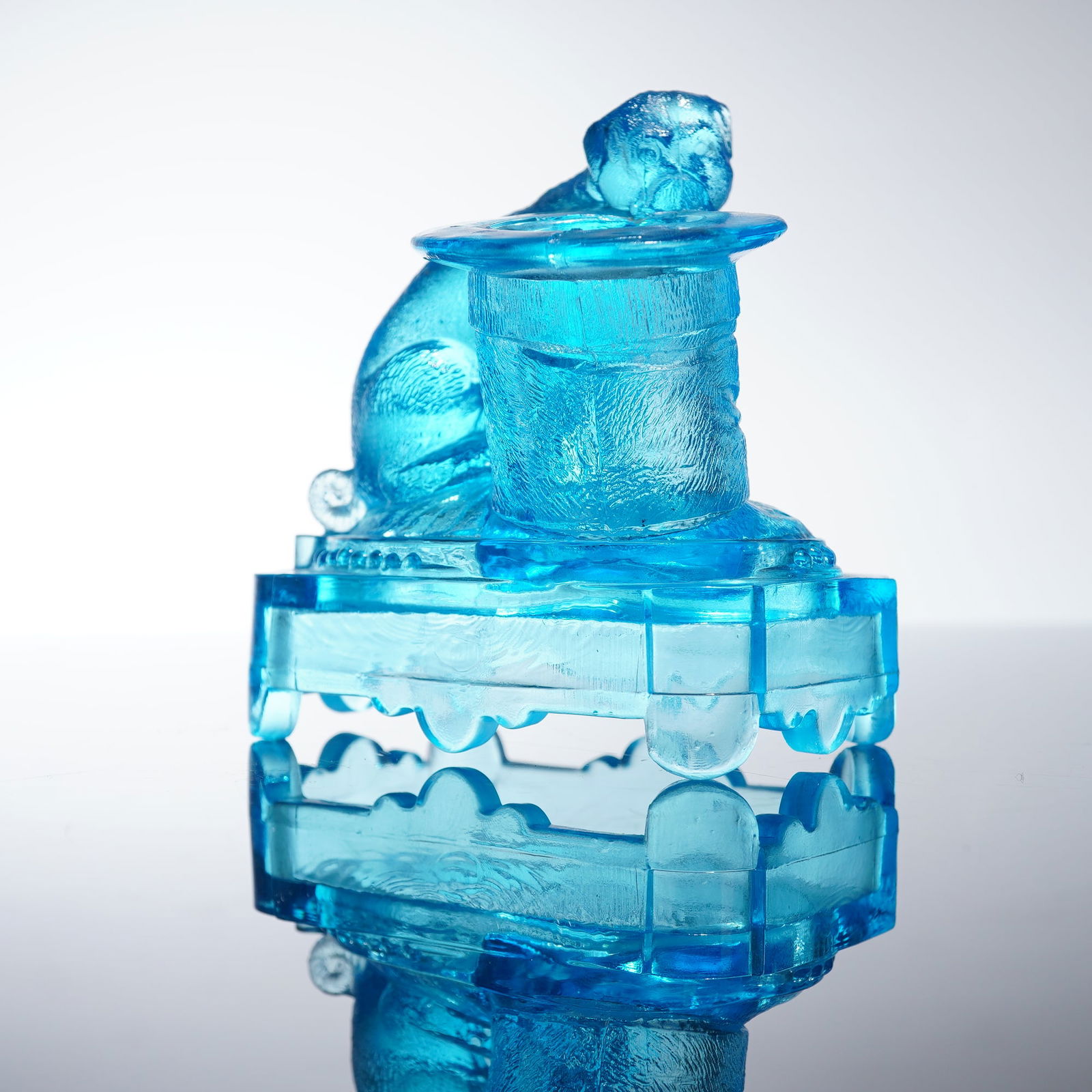 Bellmont Glass EAPG Matchstick Holder, Bulldog with Top Hat: The holder is executed in translucent turquoise-blue pressed glass. With the rectangular base featuring scalloped lower edges and stylized feet. The fitted lid is surmounted by a figural element depic