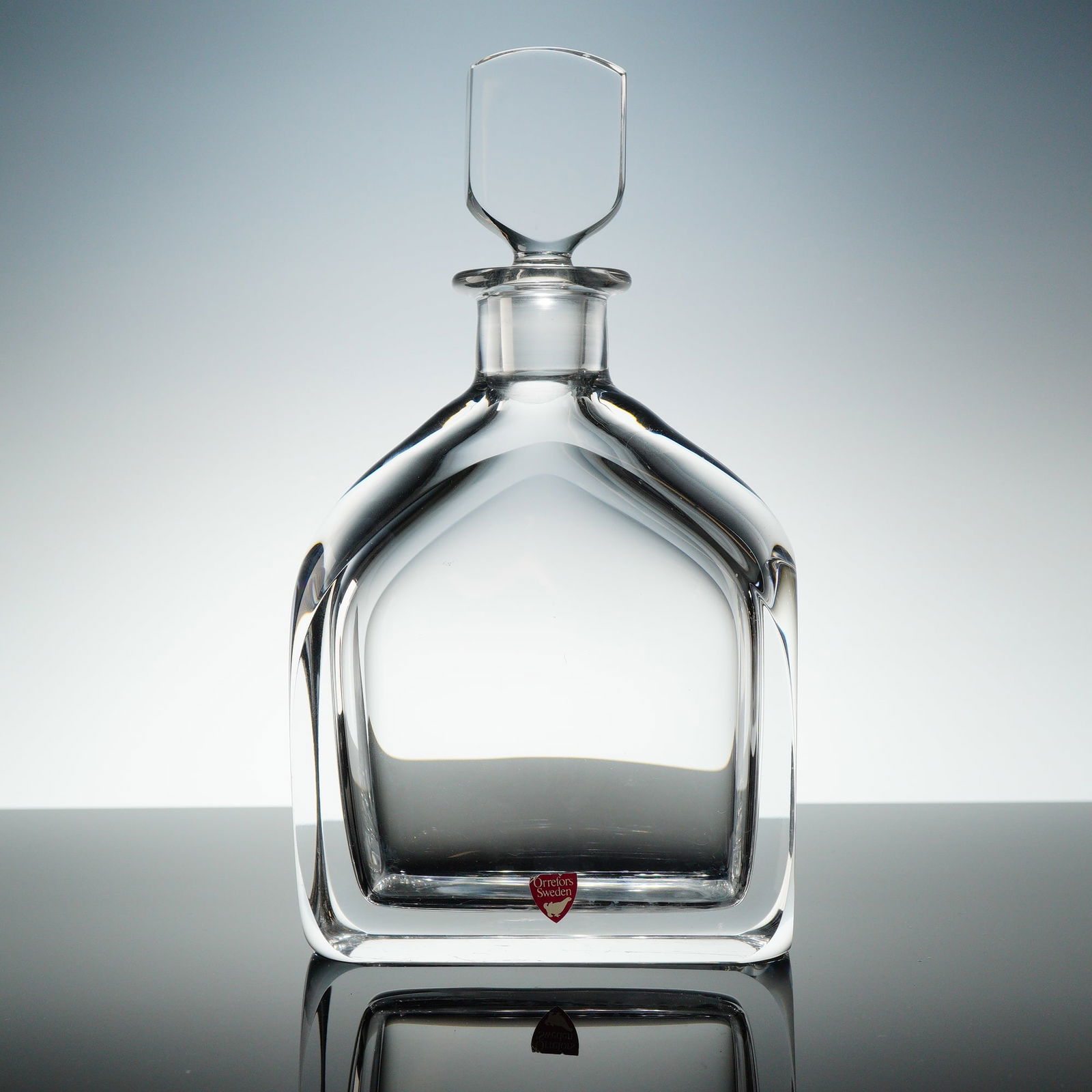 Orrefors Crystal Decanter with Stopper: A two-piece clear crystal decanter set designed by Olle Alberius for Orrefors, Sweden. The set comprises one heavy decanter body and one complementary shield-shaped stopper. The decanter features a th