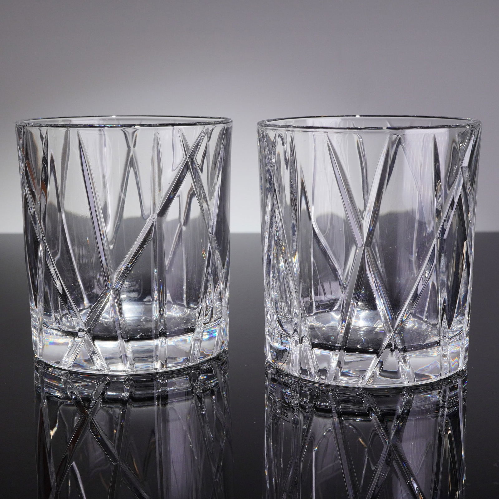 A Pair of Orrefors City Crystal Double Old Fashioned Glasses: A pair of heavy cut crystal lowball tumblers by Orrefors in City pattern. These double old fashioned glasses feature deep, extensive geometric cutting characterized by intersecting vertical and diagon