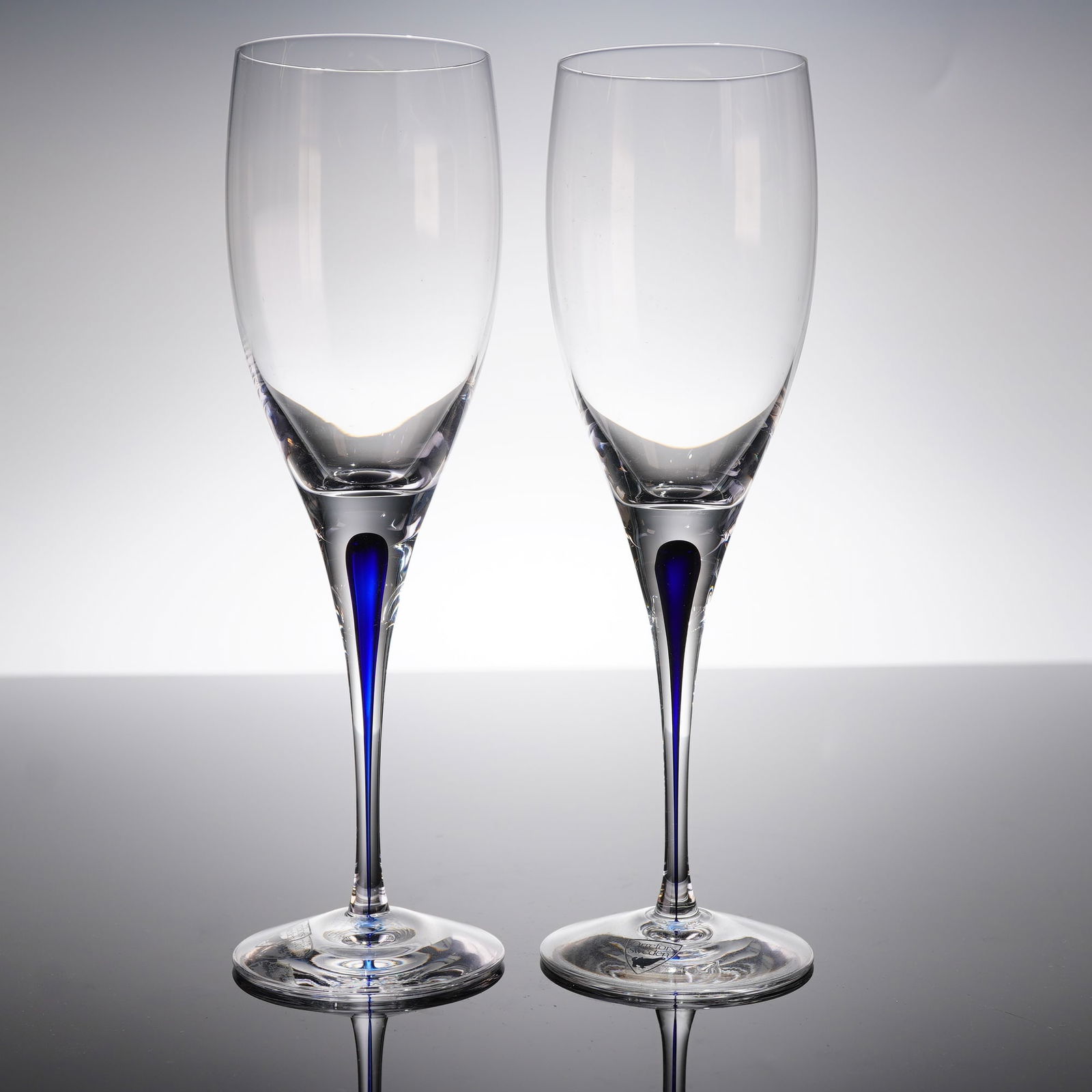 A Pair of Orrefors Intermezzo Blue Champagne Flutes: A pair of contemporary glass champagne flutes designed by Erika Lagerbielke for Orrefors, in the Intermezzo Blue patern. Each fi?ute features a tall, narrow bowl supported by an integrated stem crafte