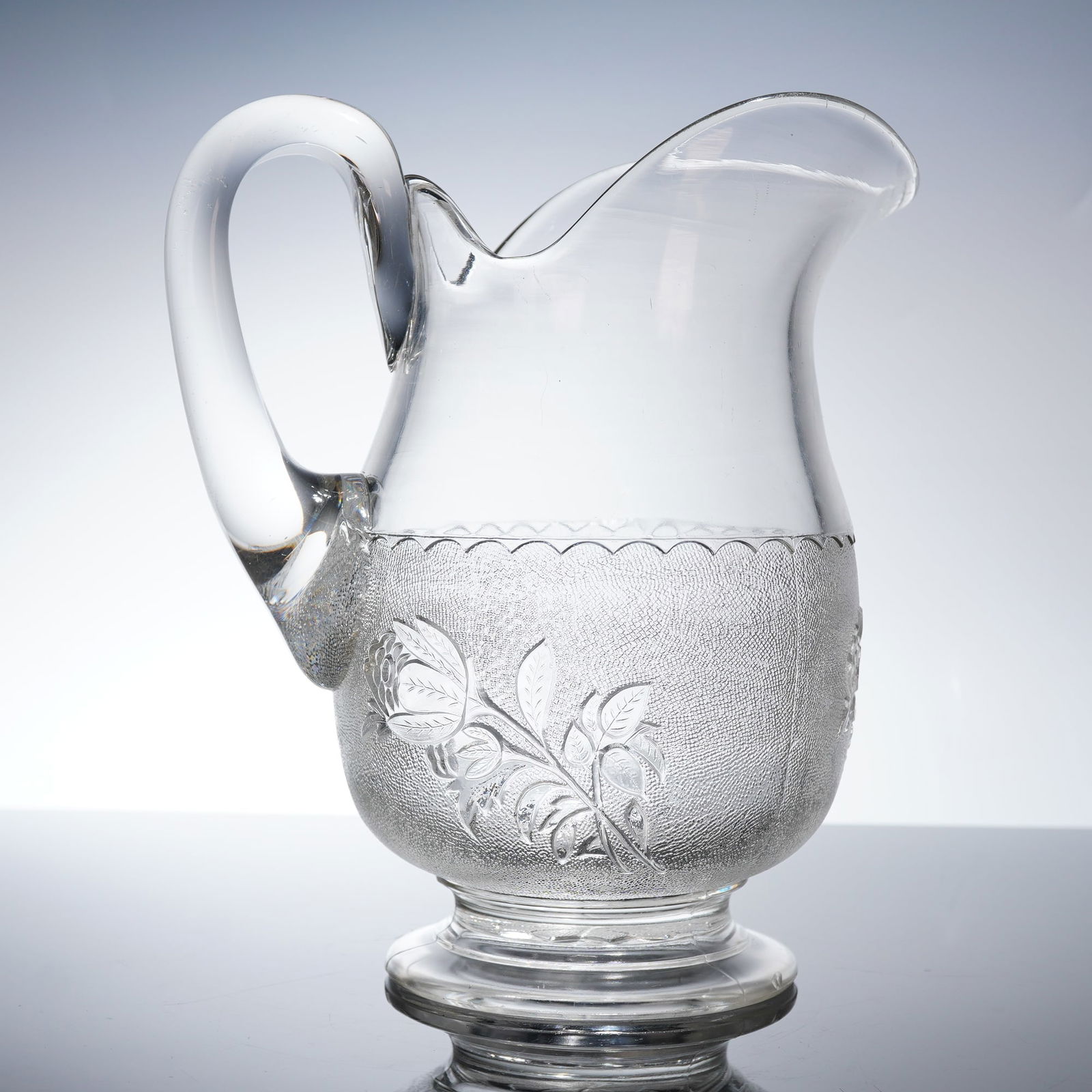 Bryce Brothers EAPG Floral Pitcher, Rose in The Snow: The form features a footed base, an applied handle, and a flared spout. The body is divided into two sections: the upper portion is plain, while the lower bulbous section is decorated. This pattern, r