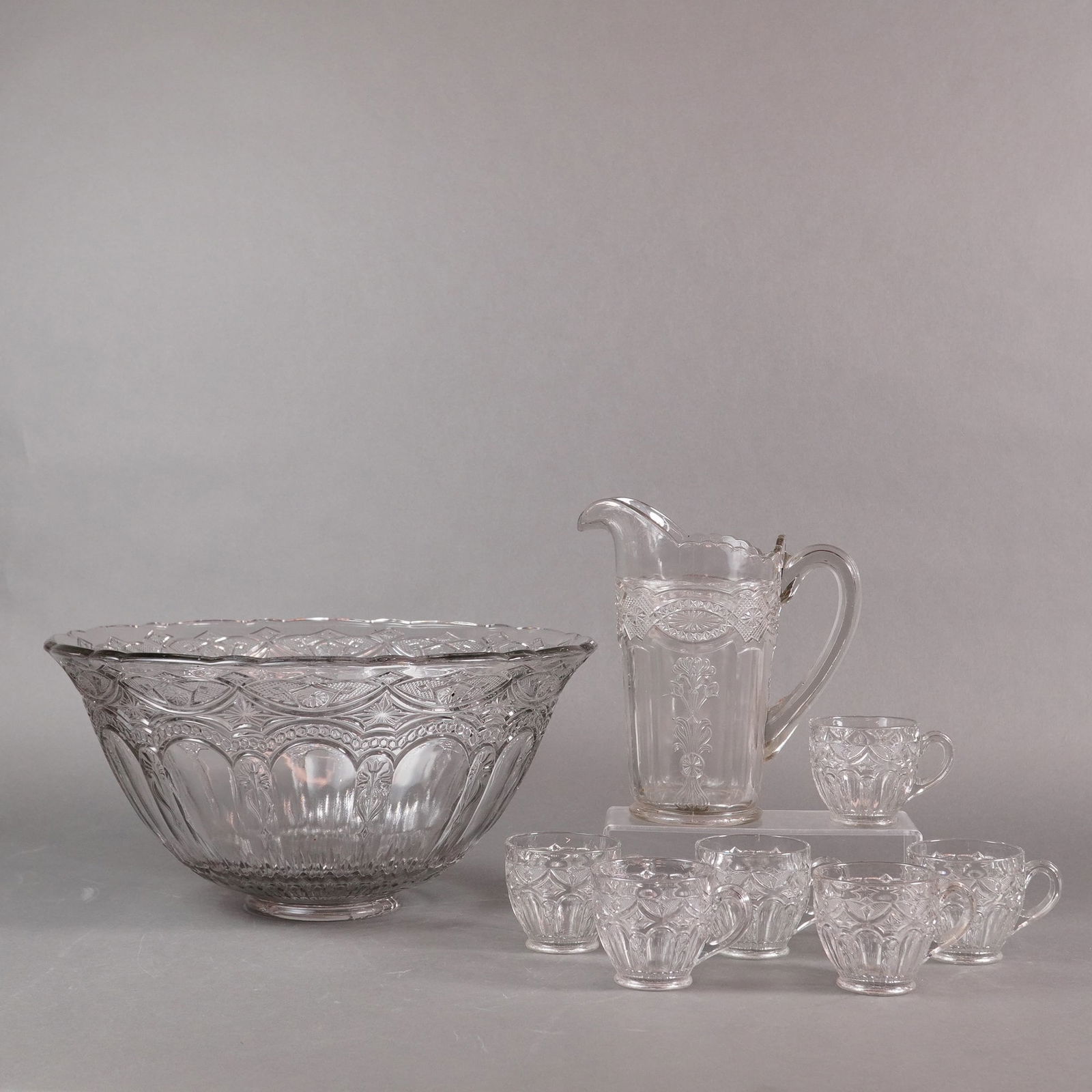 A Collection of Eight Piece EAPG Pressed Glass Punch Service Set: This is a collection of eight pieces comprising a punch service set, executed in clear pressed glass consistent with the Early American Pressed Glass (EAPG) style. The set includes one large, footed p