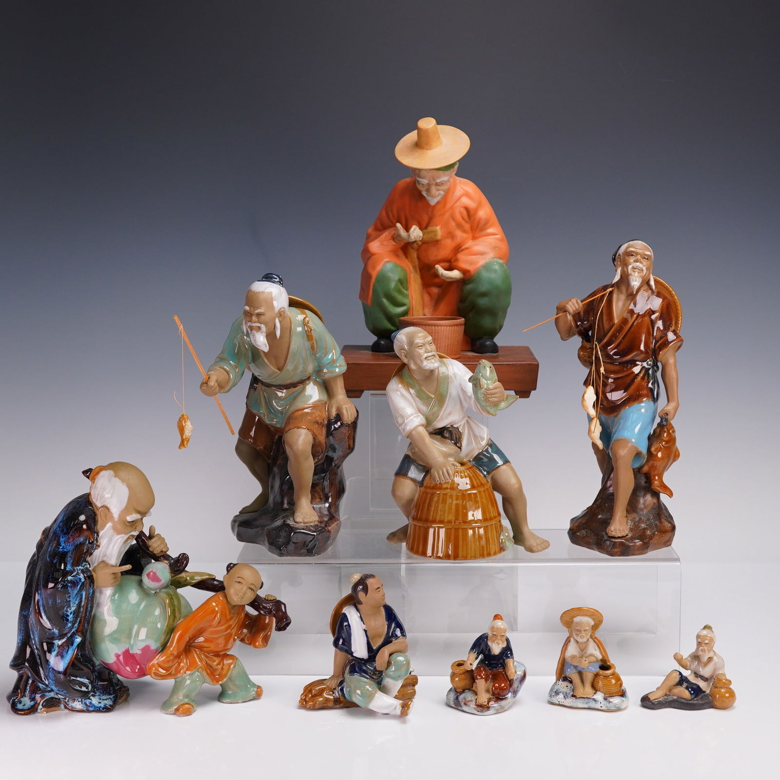 9pc Chinese Mudmen Porcelain Figurines: A colorful 9pc group of Chinese mudmen porcelain figurines, each hand-painted and depicting traditional scenes of rural life. The lot includes many elderly fishermen, captured in dynamic poses with fi