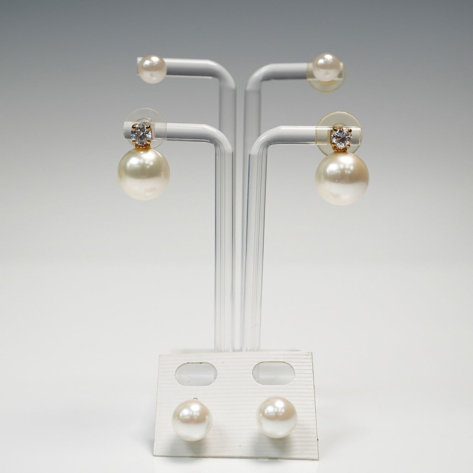 3pc Simulated Pearl Post Earrings Lot: Collection of three pairs of gold tone post earrings featuring simulated pearls. Includes one pair of drop earrings with large pearl dangles suspended from clear faux diamond studs (0.75"H), and two p