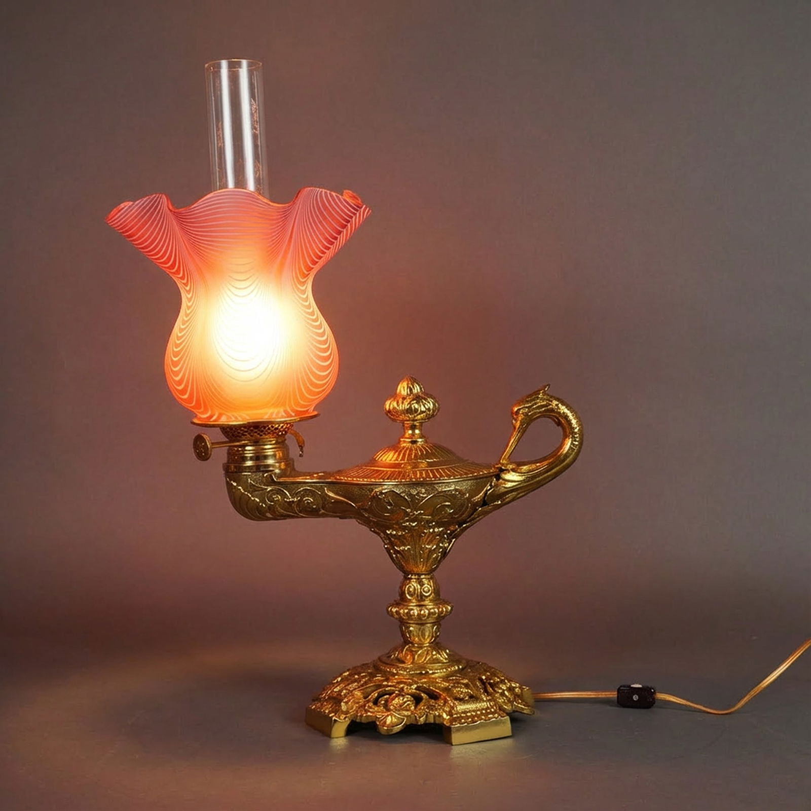 Duplex Brass Pink Swirl Glass Shade Electrical Genie Lamp: A Duplex oil lamp converted for electrical use and cast in brass in the form of a genie lamp with scrollwork and a swan-head handle, mounted on a pierced and relief-molded footed base. Fitted with a