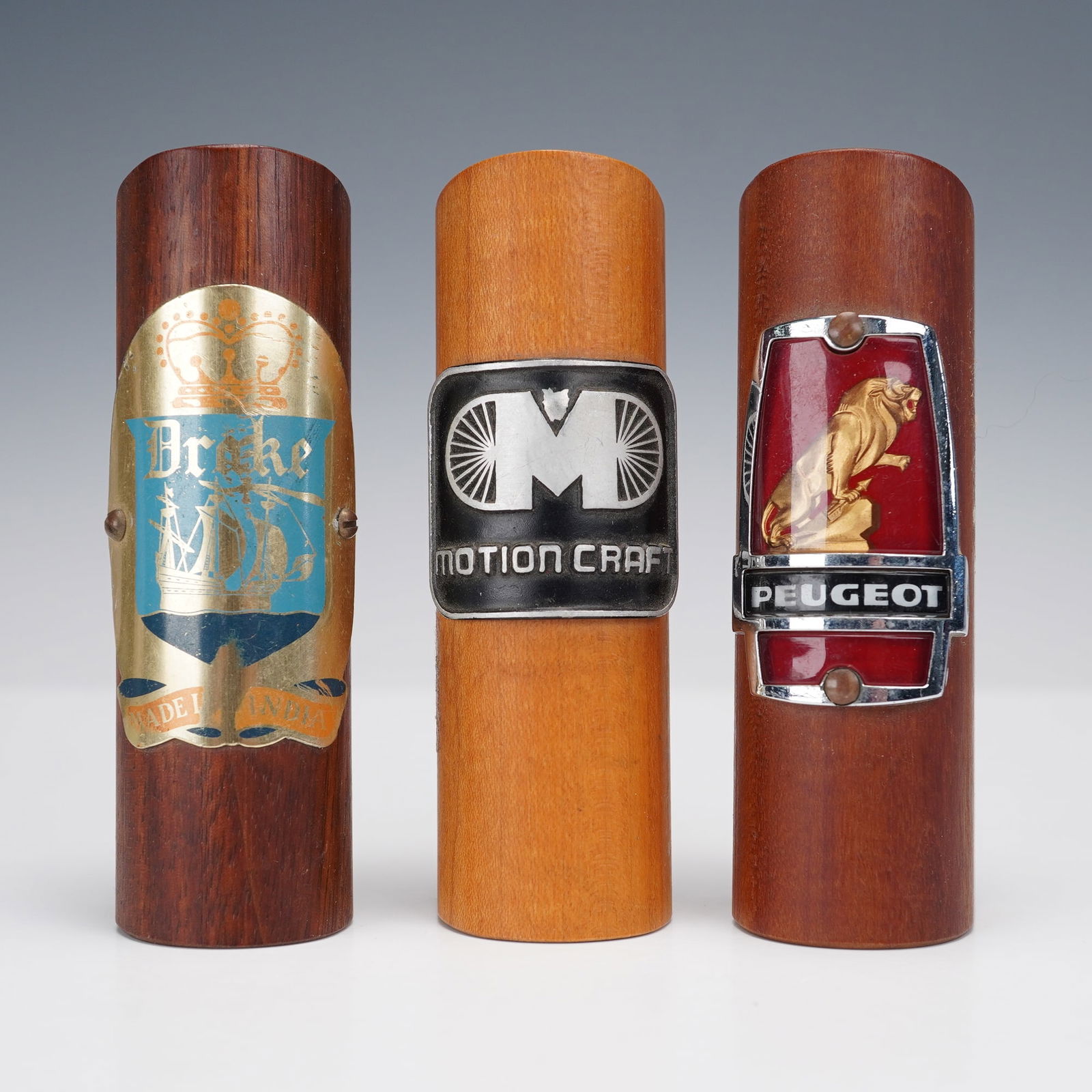 3pc Ralph W. Rogers Wooden Vehicle Emblem Displays: Set of three handcrafted wooden display blocks by Ralph W. Rogers of Lebanon, New Hampshire, featuring vintage vehicle emblems. Includes badges for Peugeot, Motion Craft, and Drake. Each block is stam
