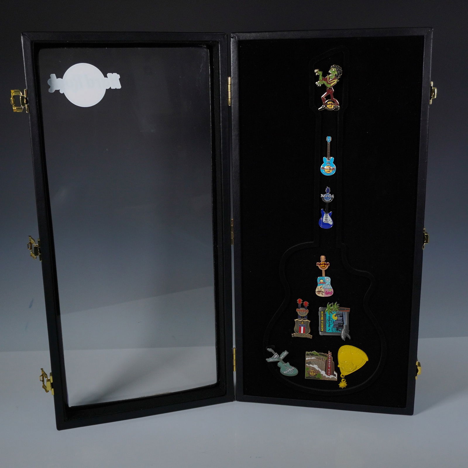 10pc Hard Rock Guitar Pin Display Case with Collectible Pins: A Hard Rock collectible guitar shaped display case containing 9 assorted enamel pins. The black faux leather case features gold tone clasps and a clear front with the Hard Rock logo. The interior is