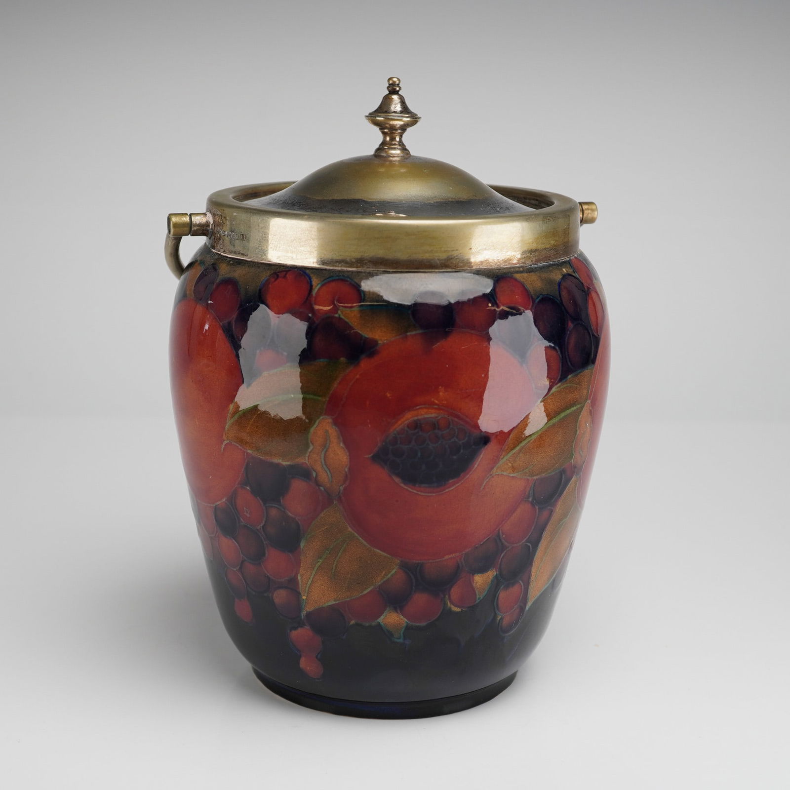 Moorcroft by William Moorcroft Silverplated Biscuit Barrel, Pomegranate: William Moorcroft biscuit barrel decorated in the Pomegranate pattern, with plated mount, swivel handle and knopped lid. The underside of the barrel is marked Moorcroft. The silverplated rim features