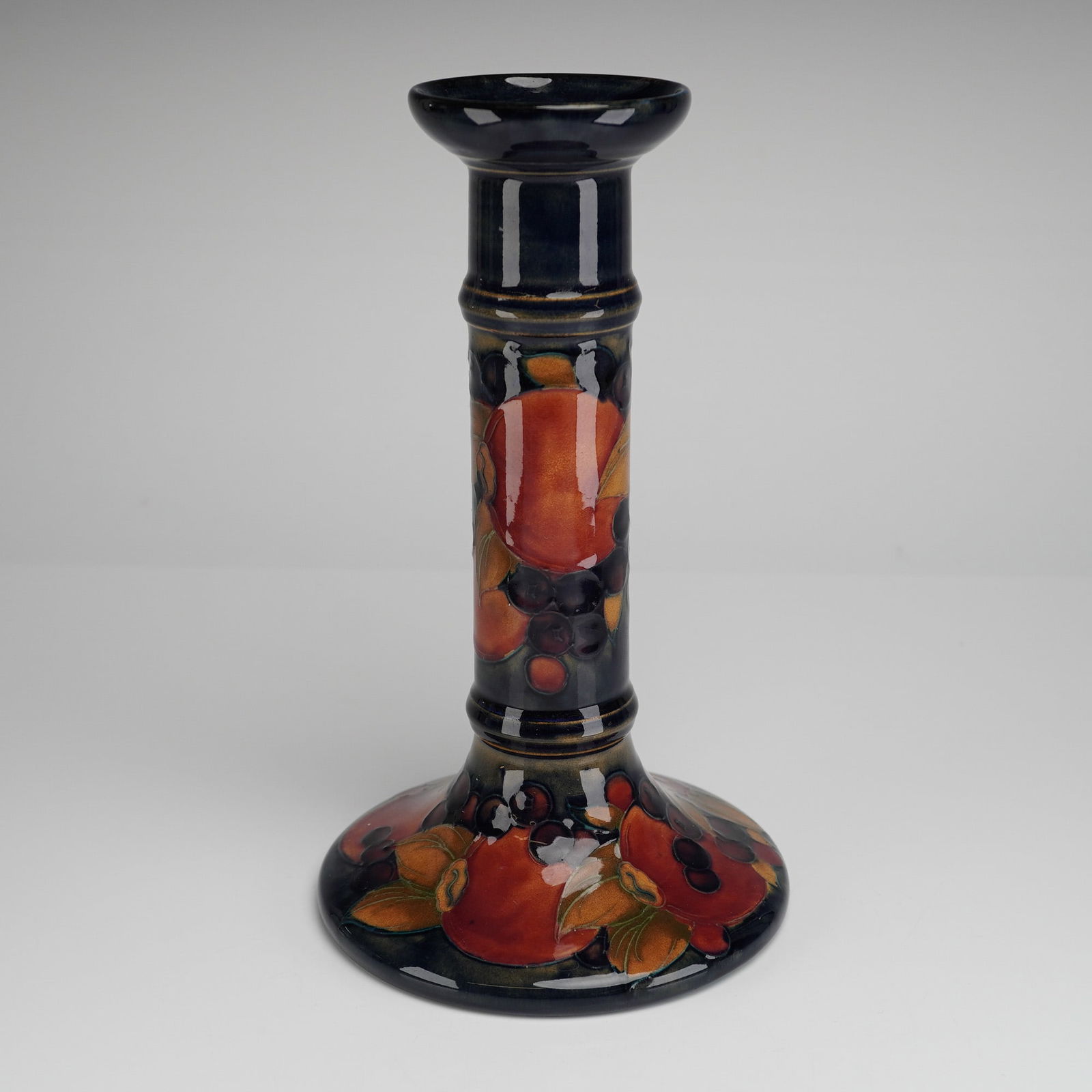 Moorcroft Pottery by William Moorcroft Candlestick, Pomegranate: William Moorcroft candlestick decorated in the Pomegranate pattern with open pomegranates to the stems, signed and impressed marks to bases Dimensions: 4.75"W x 8.25"H