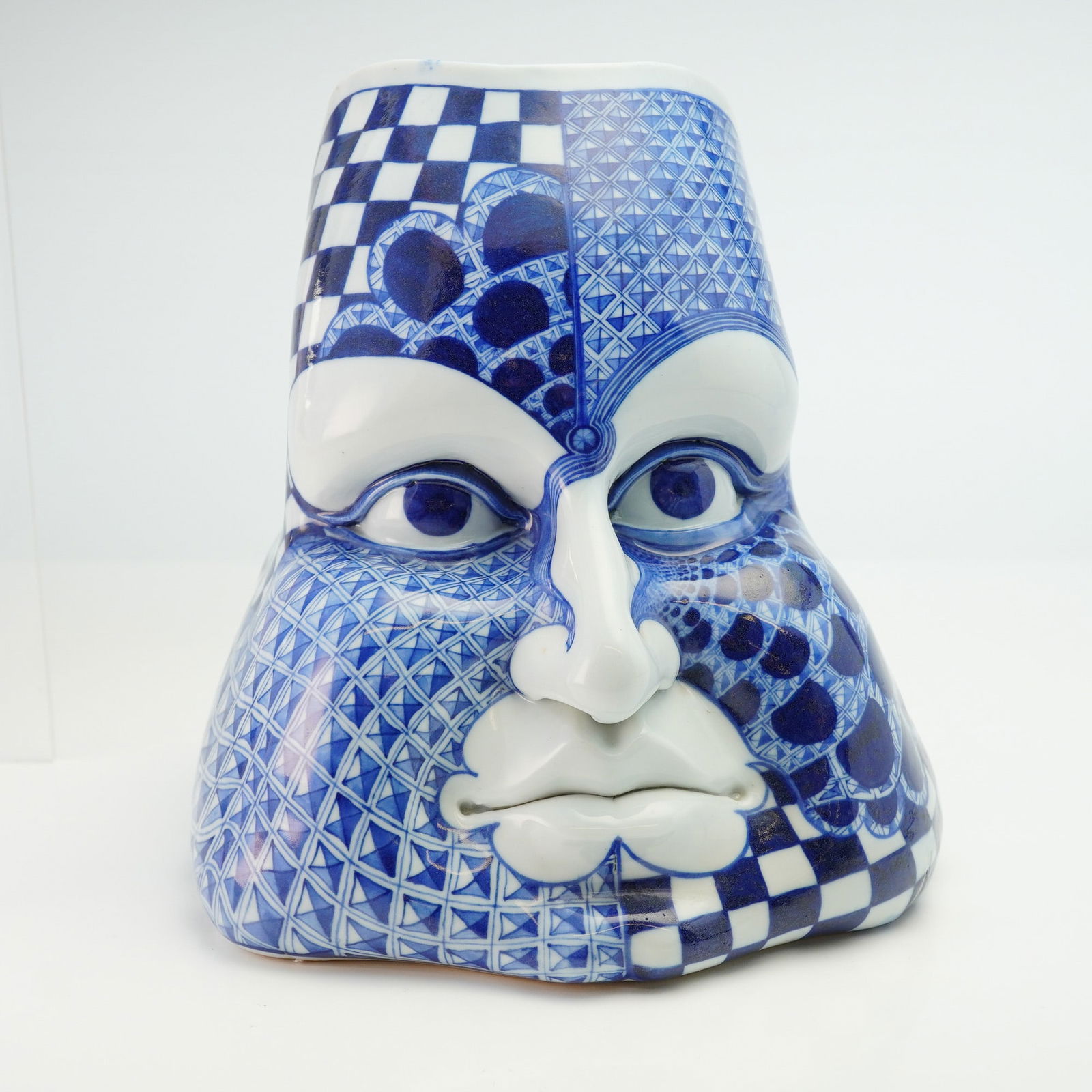 David Burnham Smith Ceramic Face Figurine: Exhibiting a complex blue and white chromatic scheme. The face is adorned with a variety of intricate patterns, including repeating checkered and imbricated scale motifs. The reverse of the piece is d