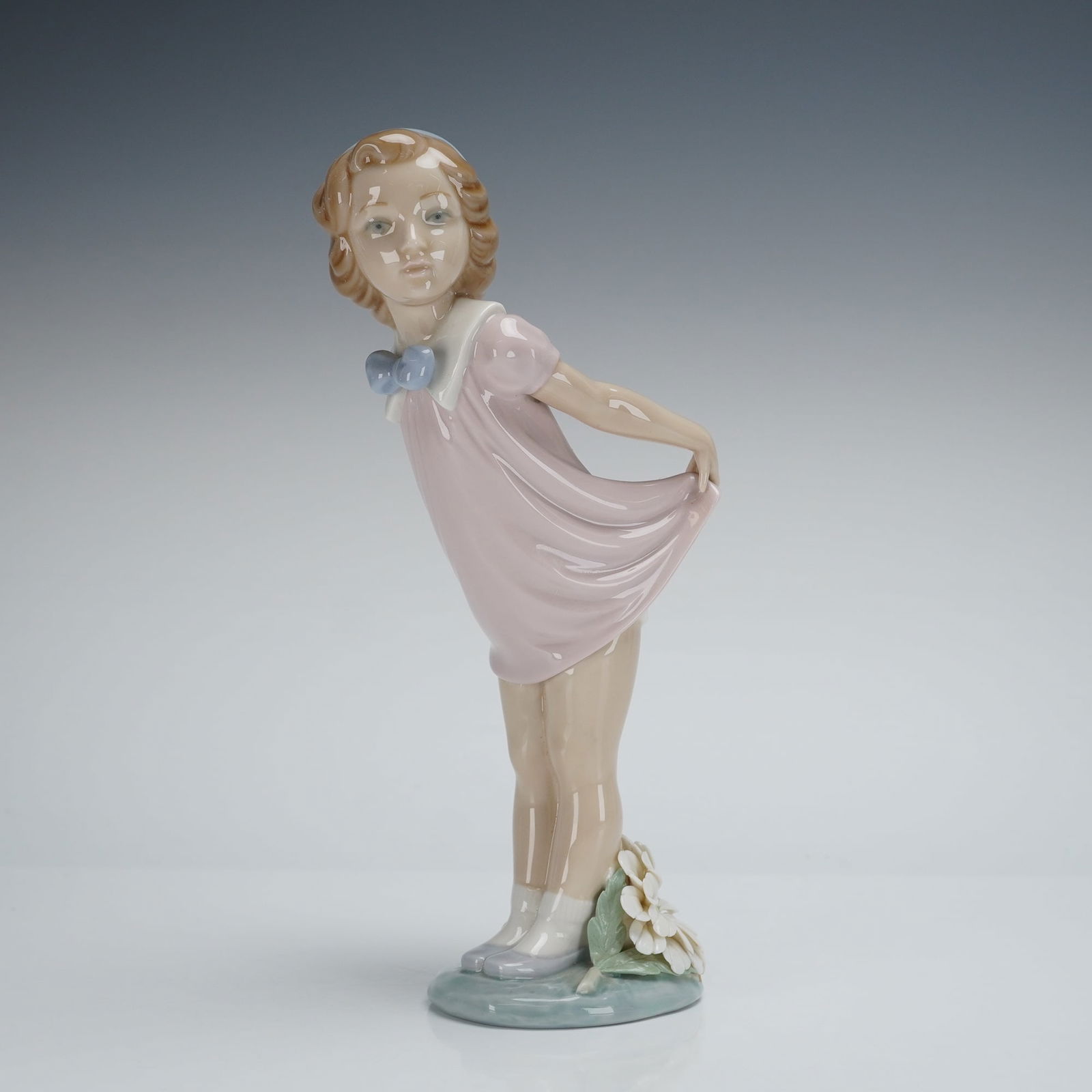 Lladro Porcelain Figurine, Girl Bowing (01005038): This high gloss glazed porcelain piece depicts a young girl in a dynamic pose, leaning slightly forward while holding up the hem of her pale pink dress. The girl wears a light blue cap and a light blu