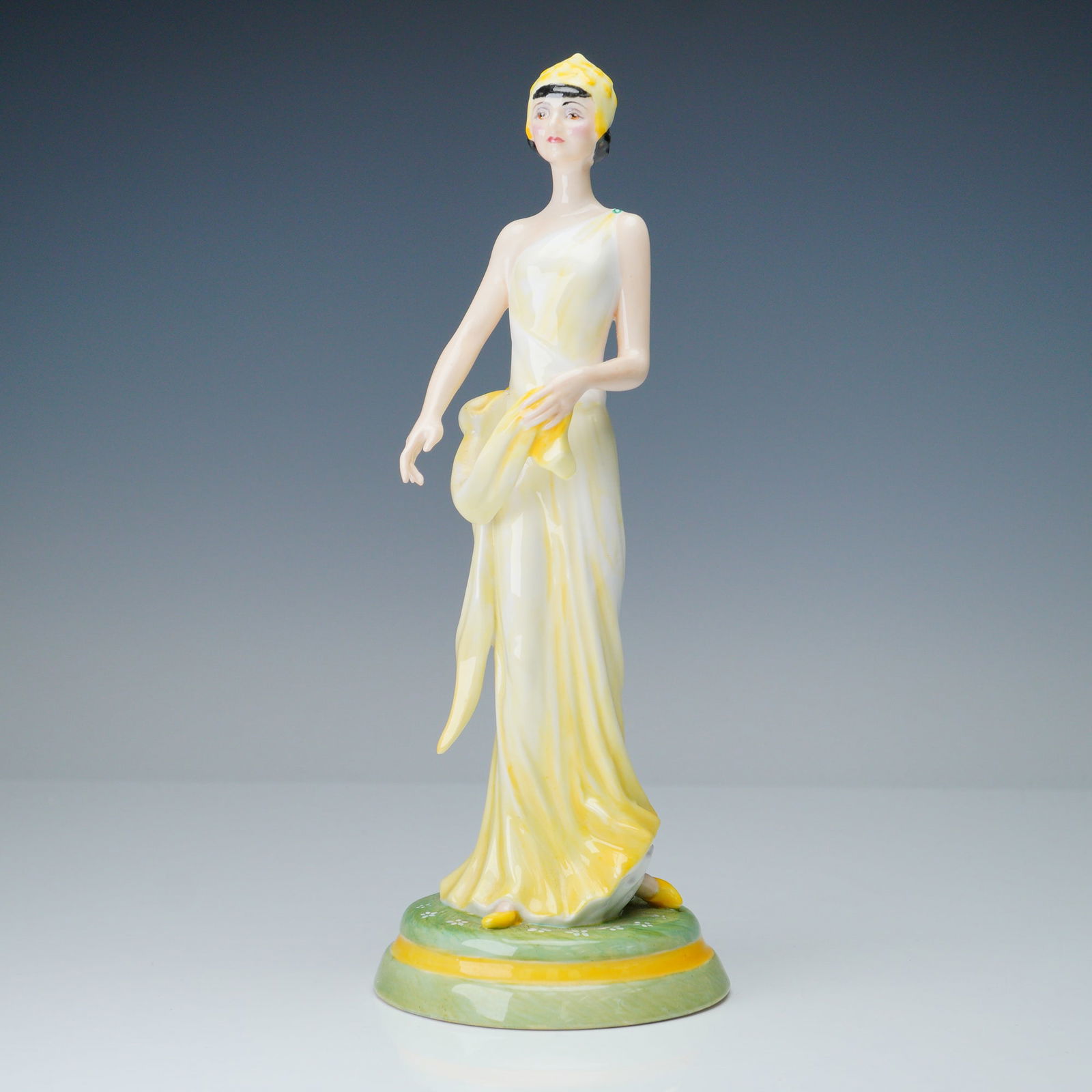 Ceramic Sculpture by Peggy Davies Figurine, Daphne: Graceful and poised, this ceramic sculpture titled Daphne by Peggy Davies presents a classically inspired female figure adorned in a flowing marbled yellow gown. The elegant lines of her robe and head